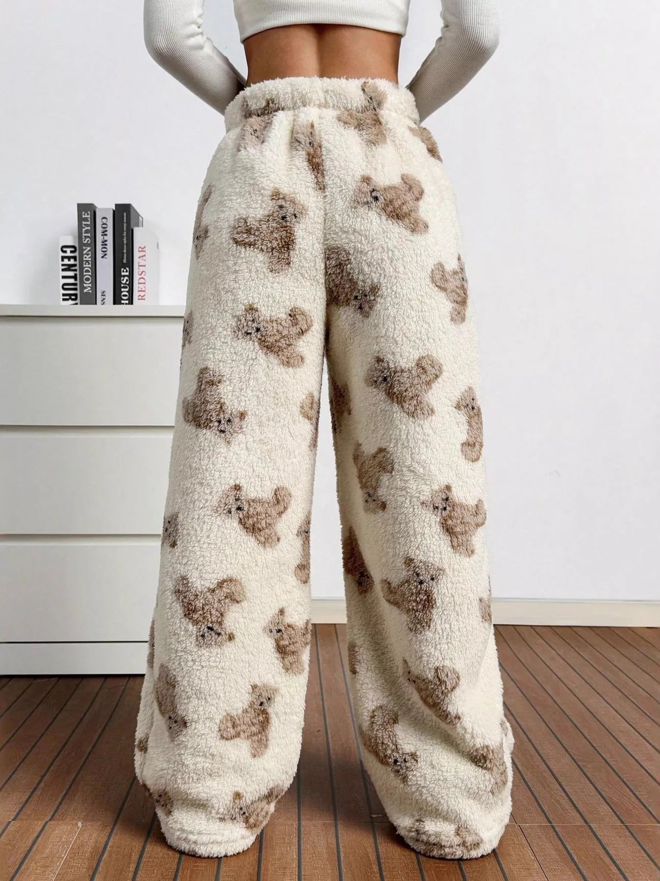 Cream plush teddy bear print lounge pants with drawstring waist, worn indoors with a white crop top near a fireplace.