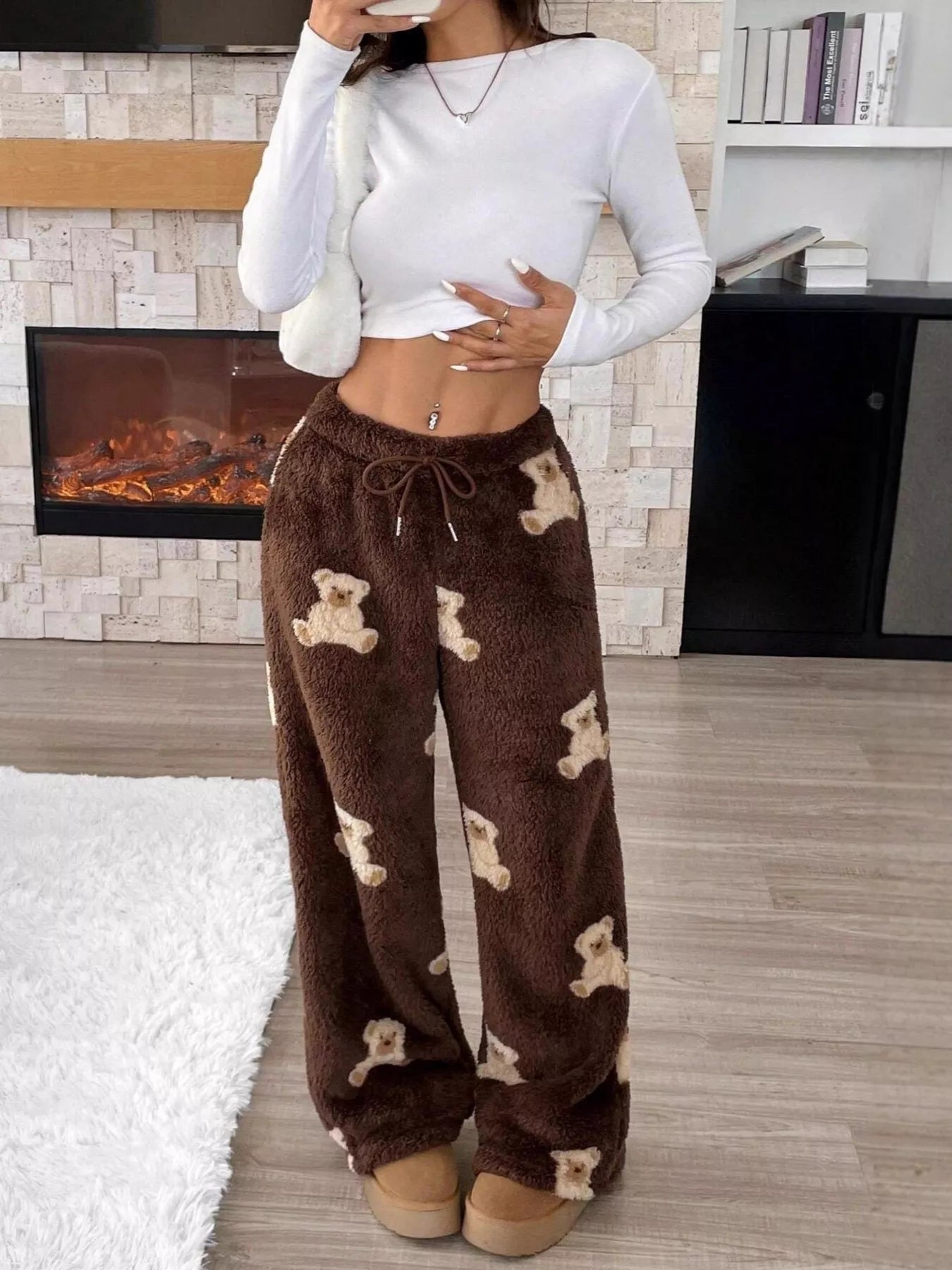 Brown plush teddy bear print lounge pants with drawstring waist, worn indoors with a white crop top near a fireplace.