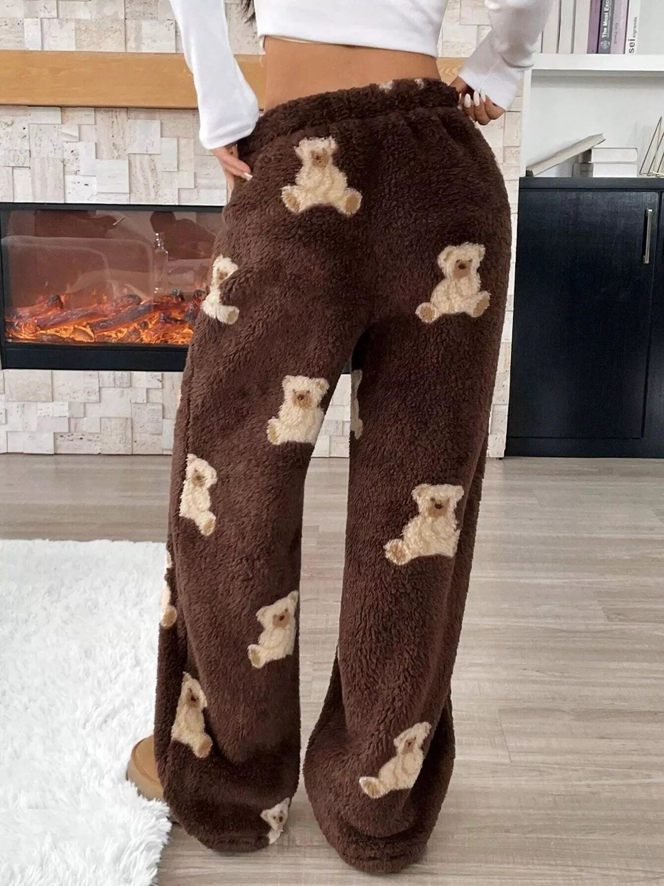 Brown plush teddy bear print lounge pants with drawstring waist, worn indoors with a white crop top near a fireplace.