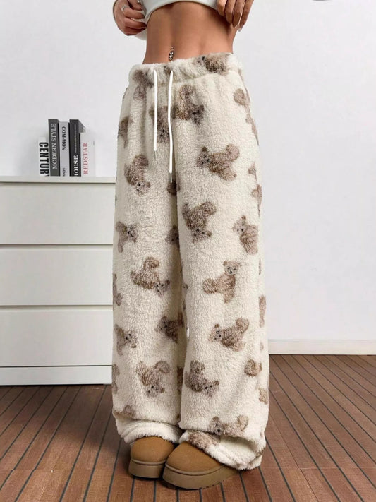 Cream fuzzy teddy bear print lounge pants with drawstring waist, styled with cozy slippers in a modern indoor setting.