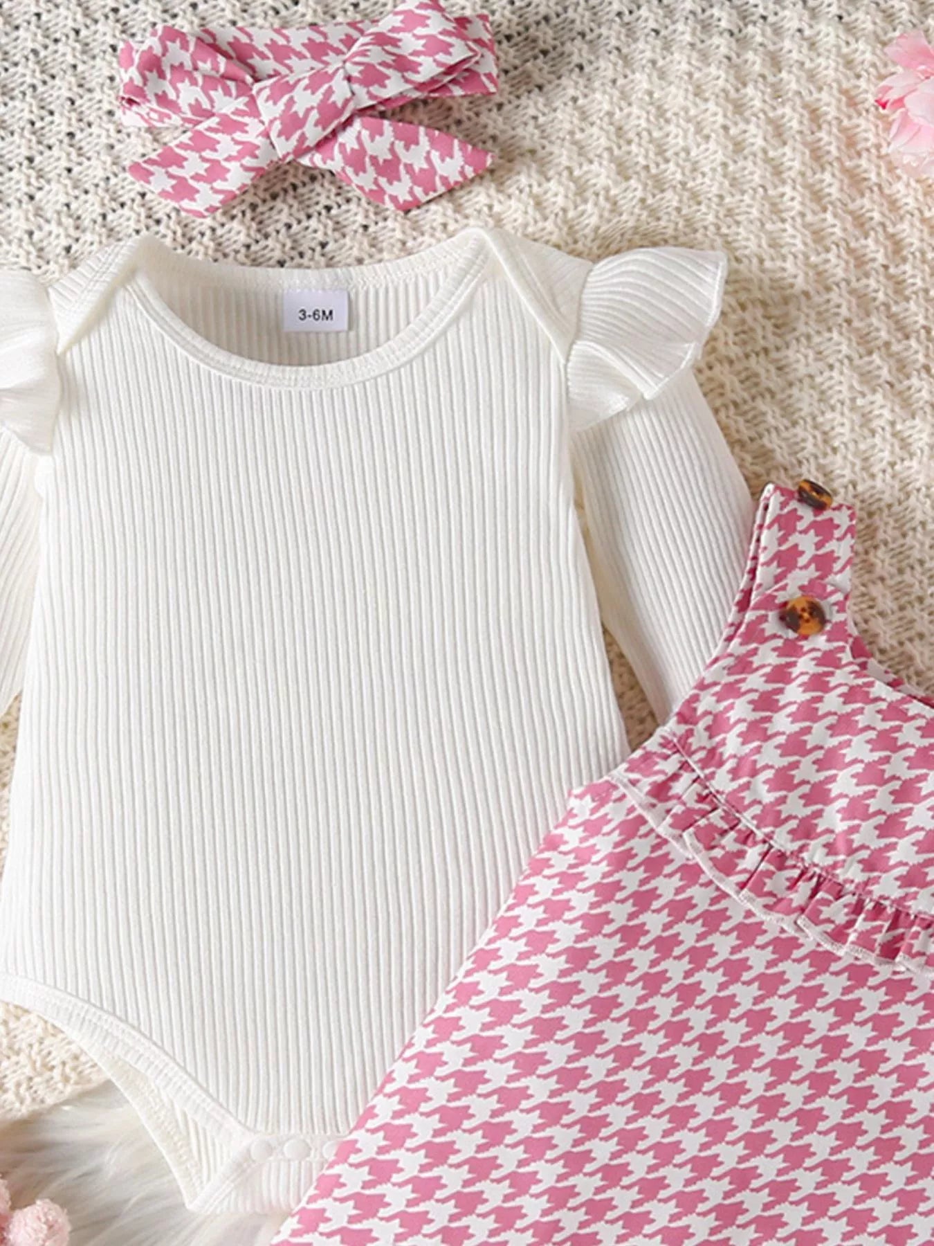 Pink houndstooth baby jumper dress with embroidered duck family and a white ruffle long-sleeve onesie, displayed with matching bow and plush toy.