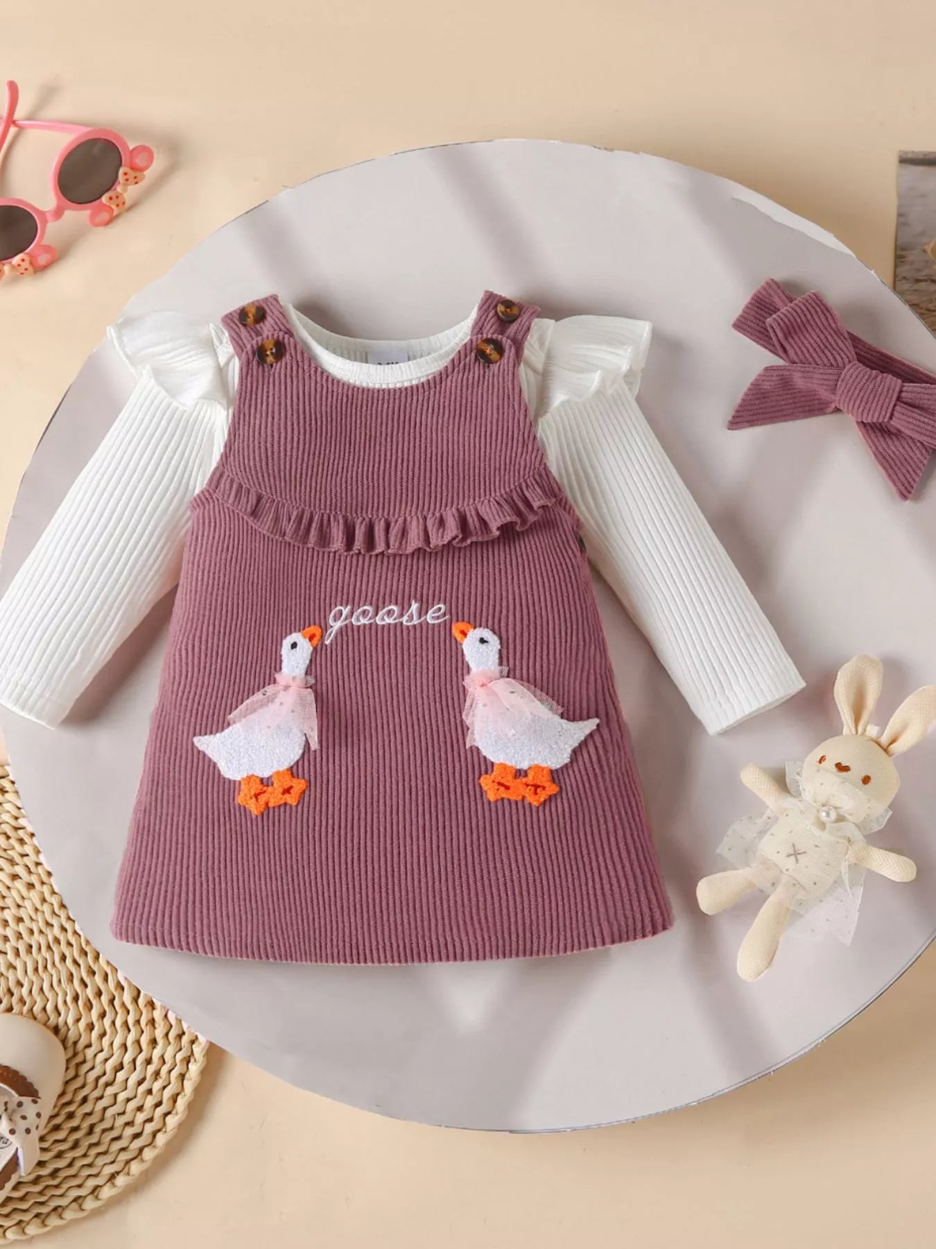 2-piece outfit with mauve corduroy jumper dress featuring embroidered geese and a white long-sleeve top, styled with matching bow and accessories.