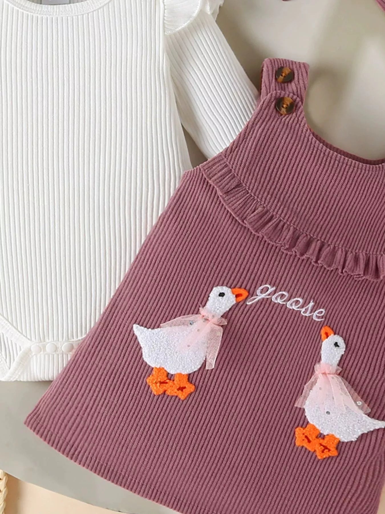 2-piece outfit with mauve corduroy jumper dress featuring embroidered geese and a white long-sleeve top, styled with matching bow and accessories.