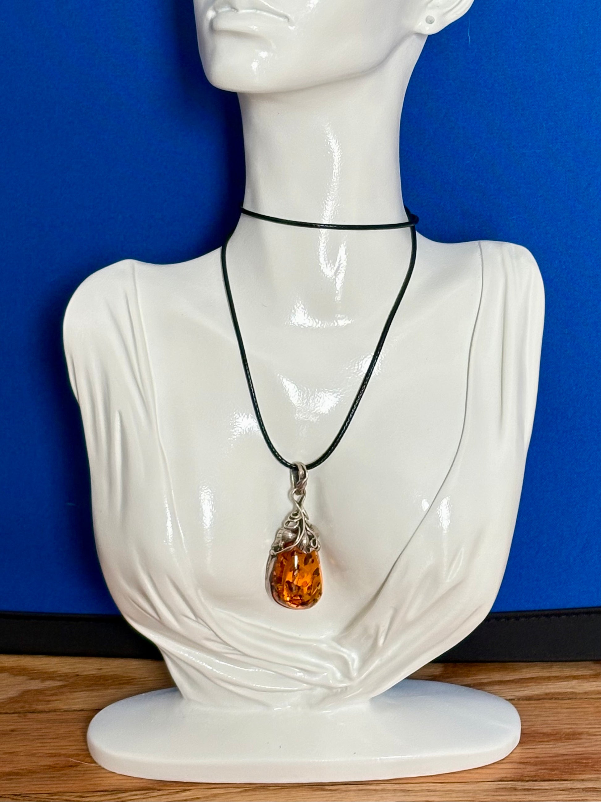 Mannequin bust wearing a necklace with an amber pendant against a blue background