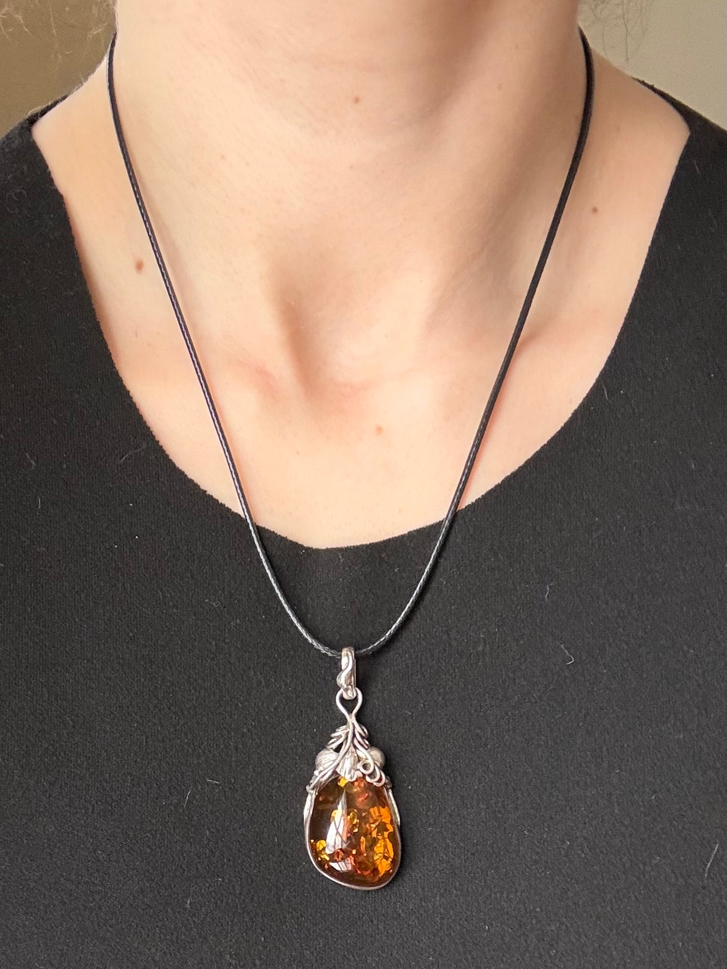 Amber pendant necklace on a black cord worn by a person against a neutral background