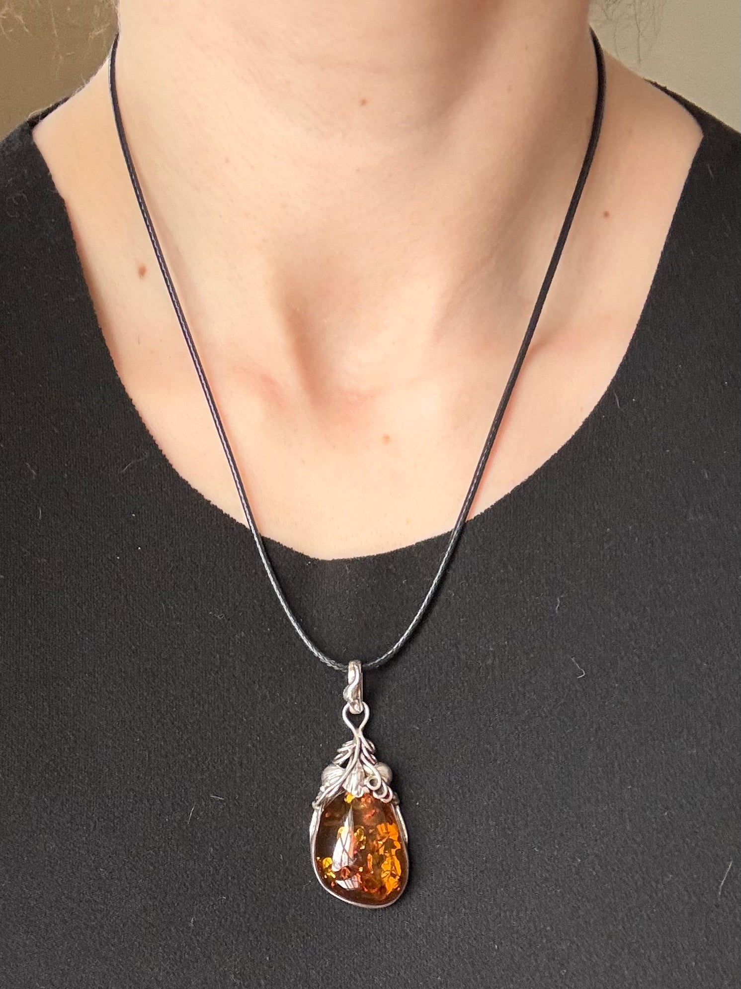 Amber pendant necklace on a black cord worn by a person against a neutral background