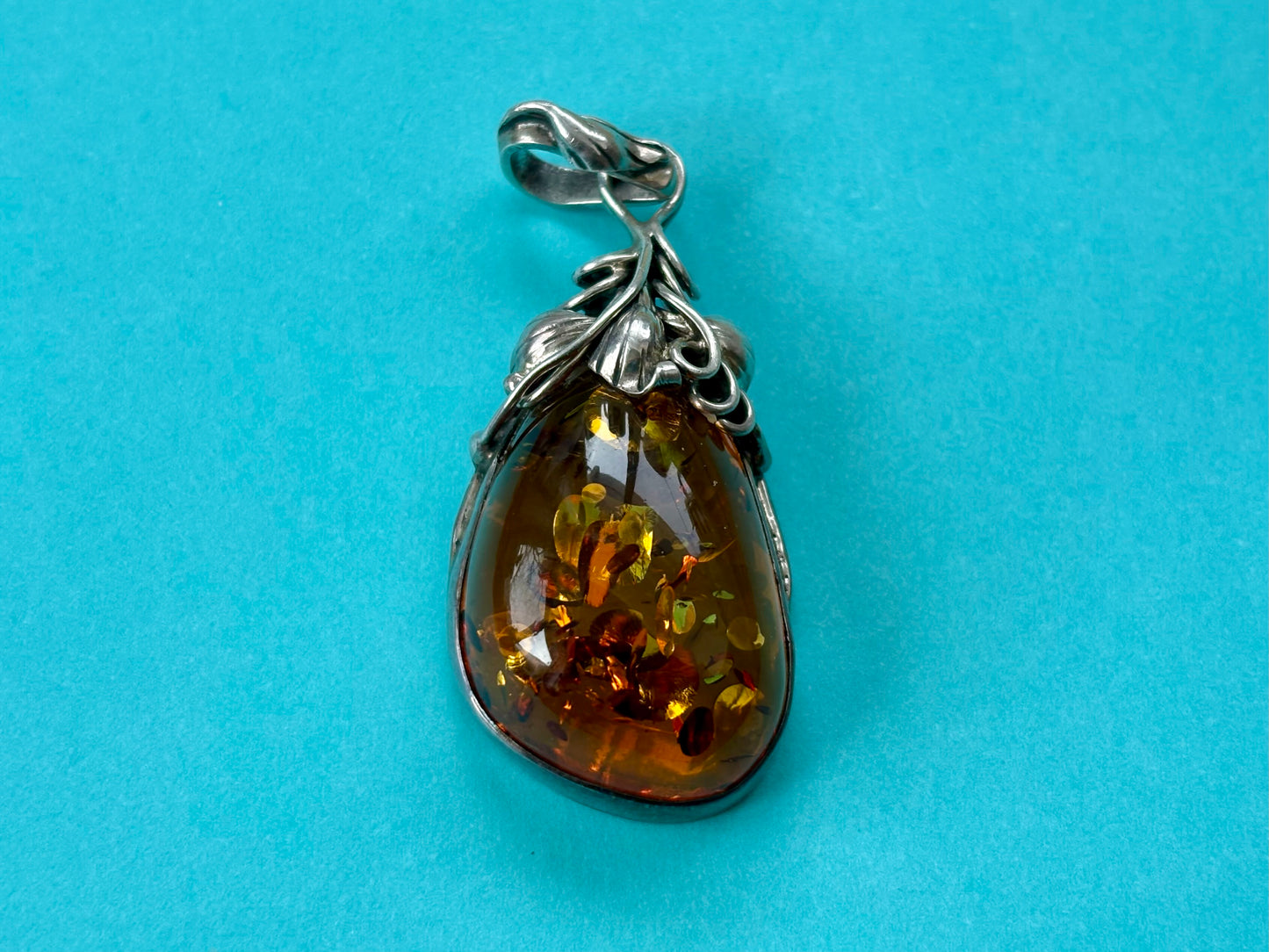 Teardrop-shaped amber pendant with silver setting on a blue background