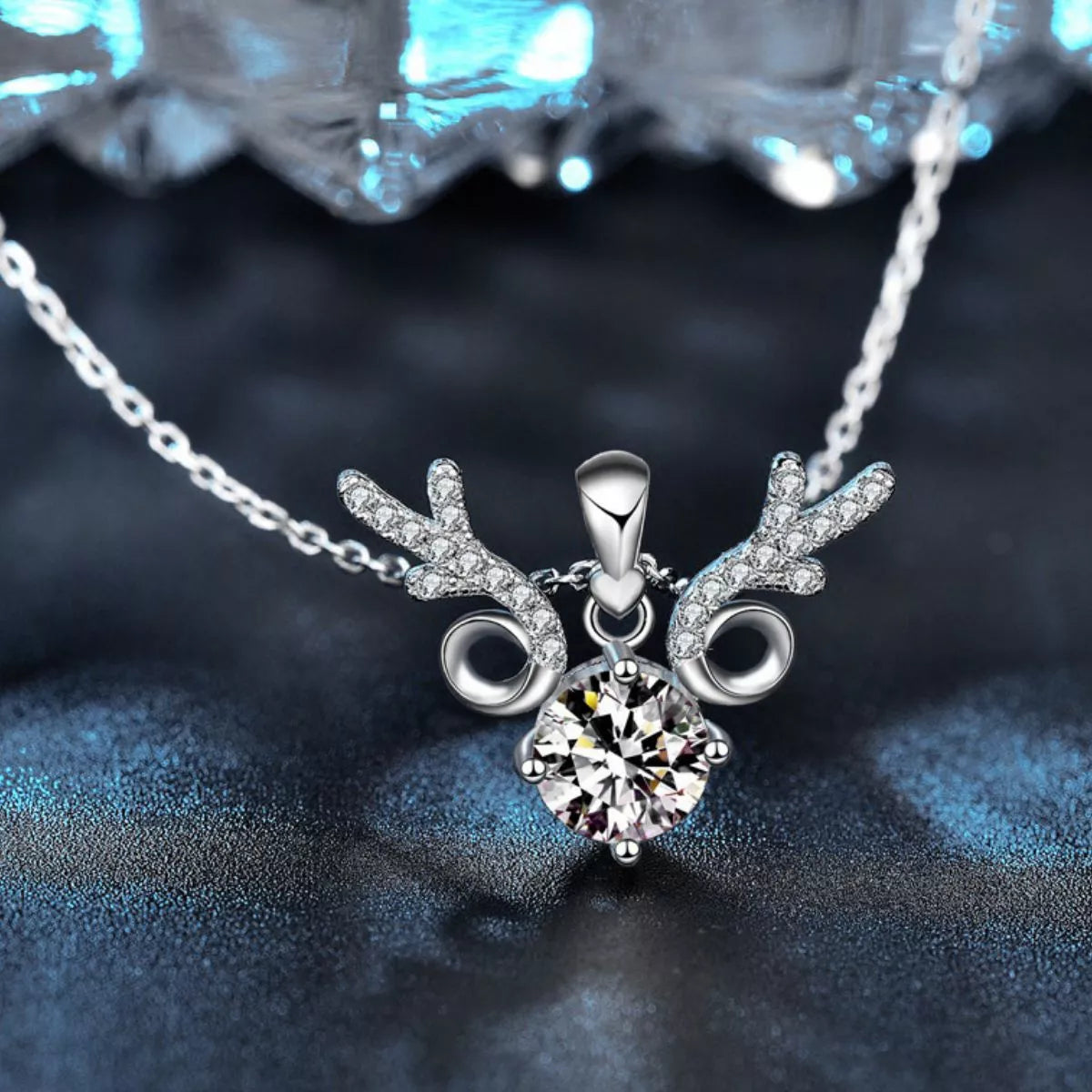 Close-up of a silver reindeer-inspired necklace with sparkling antler details and a round 1-carat moissanite center stone on a silver chain.