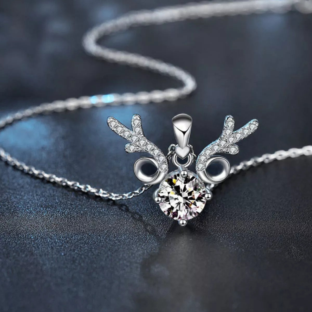 Close-up of a silver reindeer-inspired necklace with sparkling antler details and a round 1-carat moissanite center stone on a silver chain.