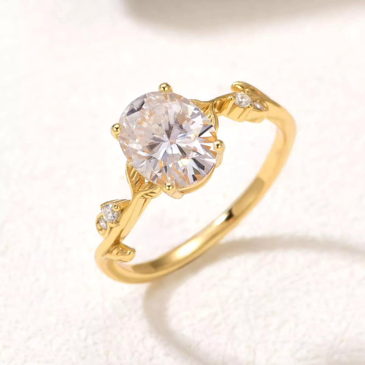 Gold oval moissanite ring with vine-like band and small zircon accents displayed in a blush jewelry box.