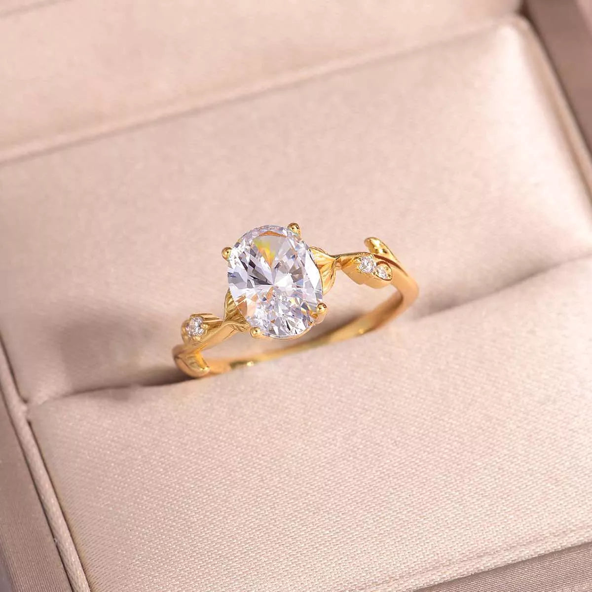 Gold oval moissanite ring with vine-like band and small zircon accents displayed in a blush jewelry box.