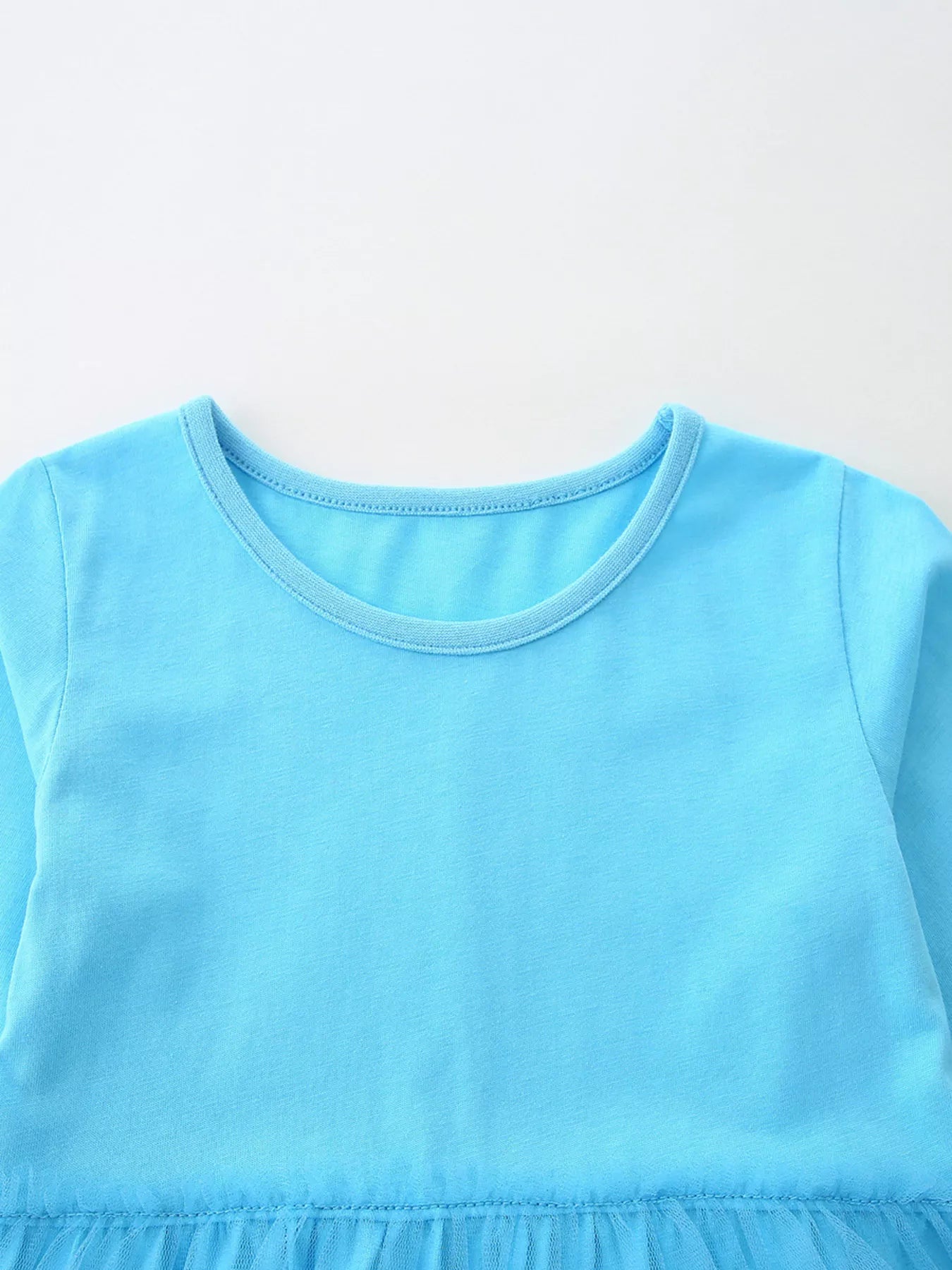 A little girl wearing a light blue long-sleeve dress with snowman, Christmas tree, and bird appliqués on a mesh skirt overlay.