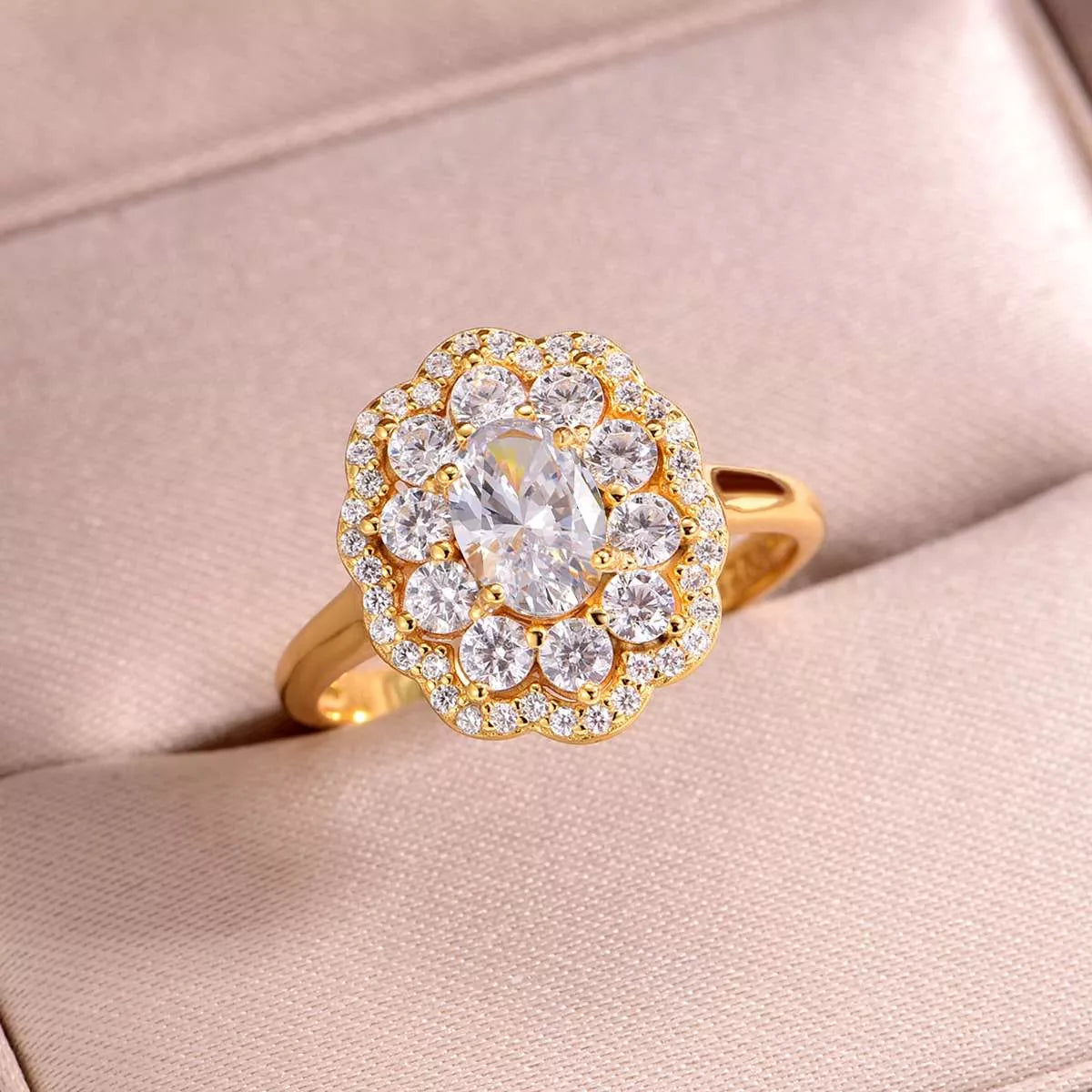 Gold-plated floral halo moissanite ring with oval center stone and layered petals of sparkling gems, displayed in a soft blush jewelry box.
