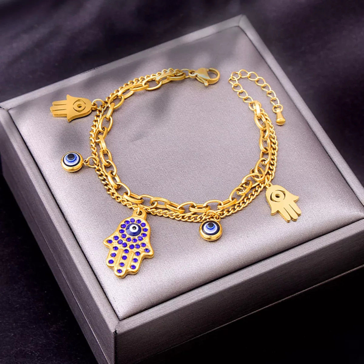 Gold-plated 3-piece jewelry set featuring a Hamsa hand charm bracelet, matching Hamsa earrings, and Evil Eye accents with blue zircon detailing on a white background.