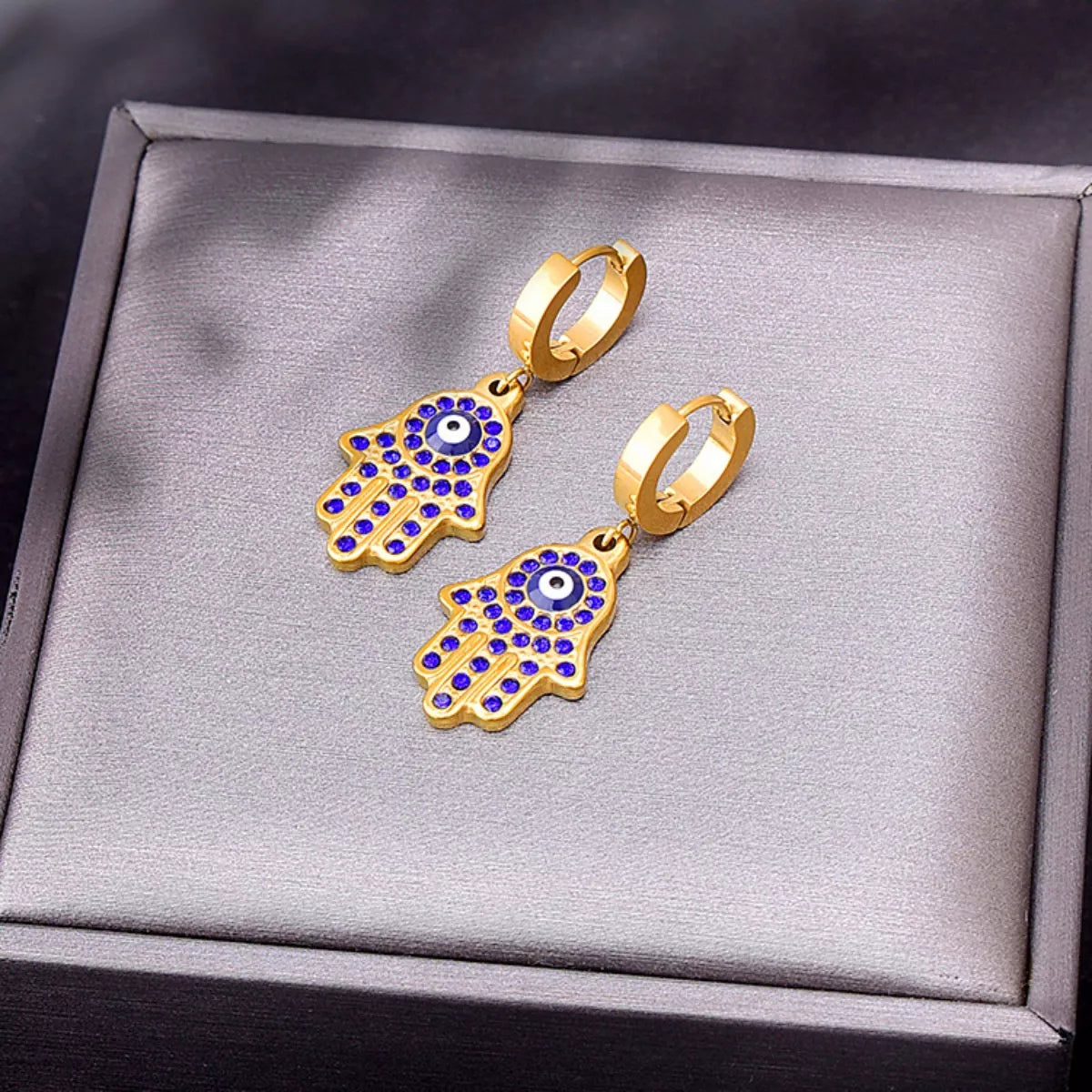 Gold-plated 3-piece jewelry set featuring a Hamsa hand charm bracelet, matching Hamsa earrings, and Evil Eye accents with blue zircon detailing on a white background.