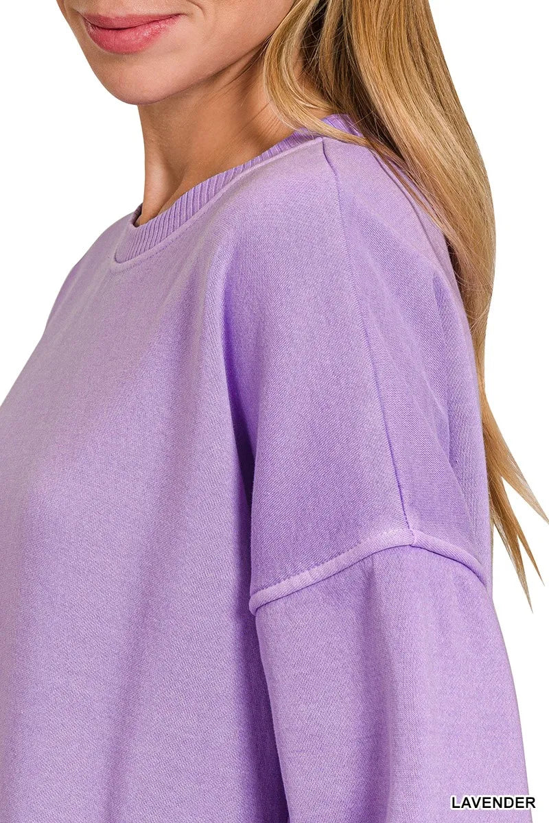 Woman wearing an oversized lavender pullover sweatshirt with contrast white stitching and balloon sleeves.