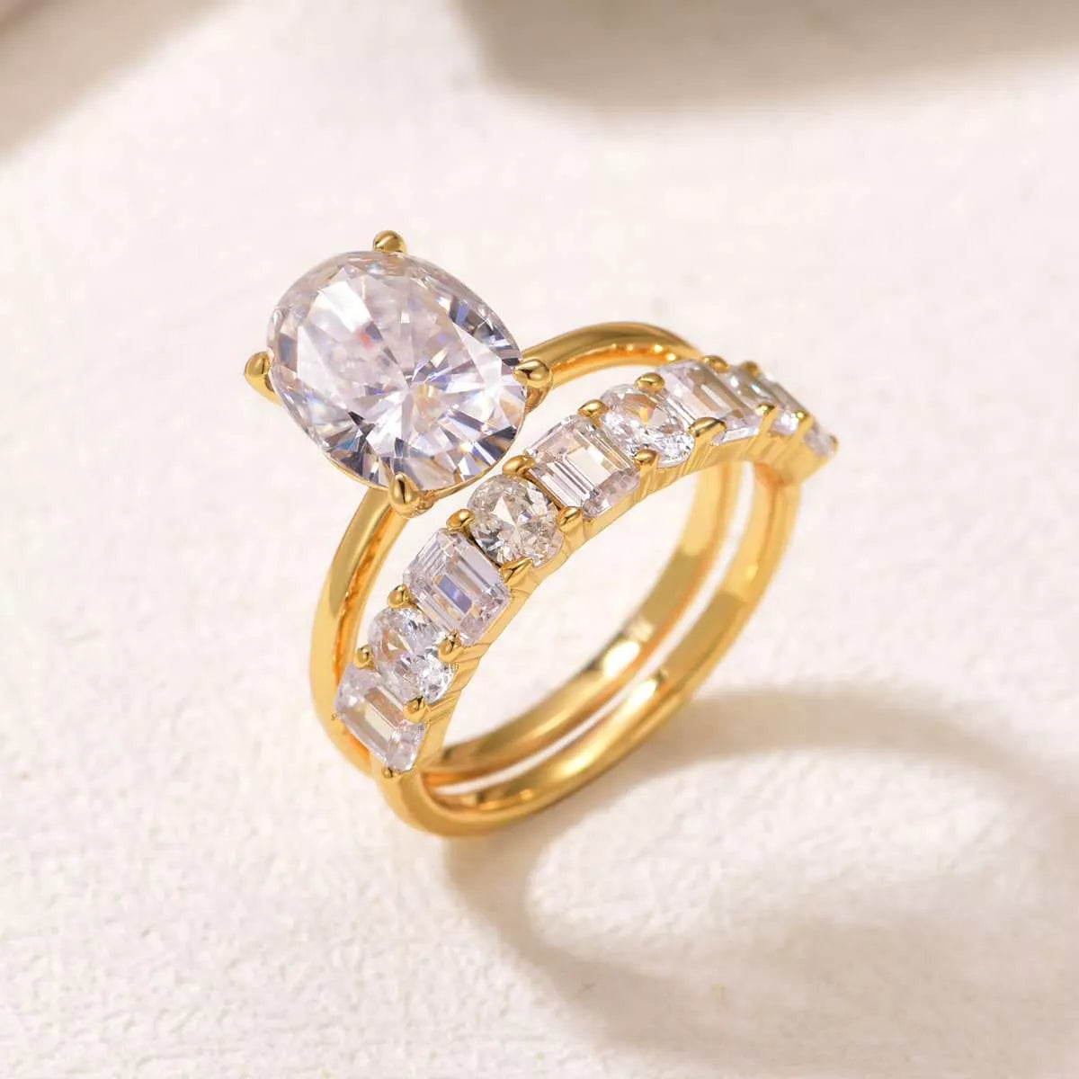 Gold two-piece oval moissanite ring set with eternity band inlaid with emerald and round cuts — elegant bridal jewelry from A Whimsical Affair.