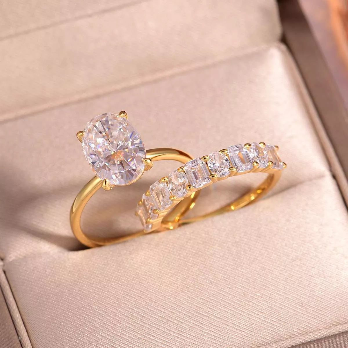 Gold two-piece oval moissanite ring set with eternity band inlaid with emerald and round cuts — elegant bridal jewelry from A Whimsical Affair.