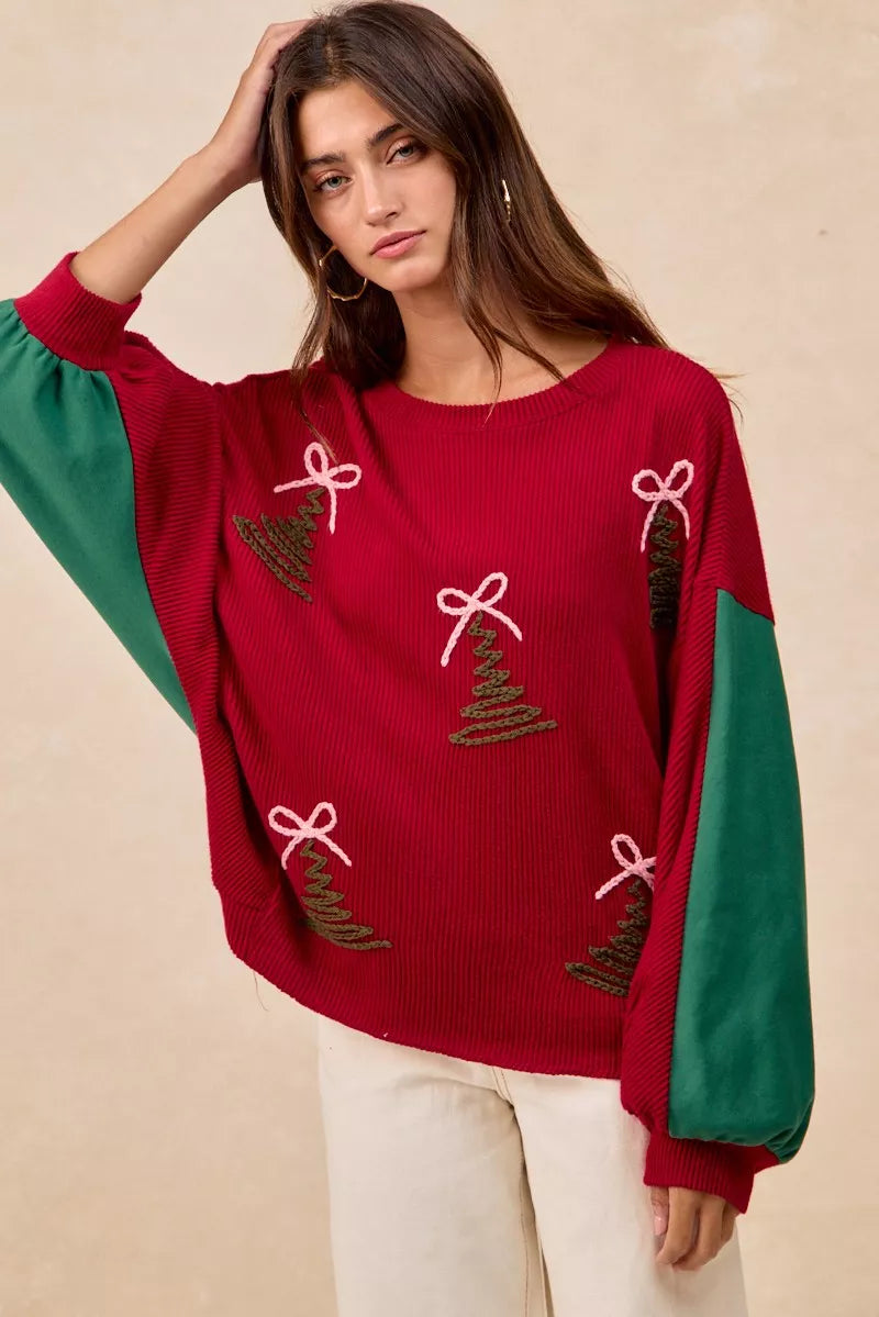Woman wearing a red Christmas sweater with embroidered green tree designs and contrasting green sleeves.