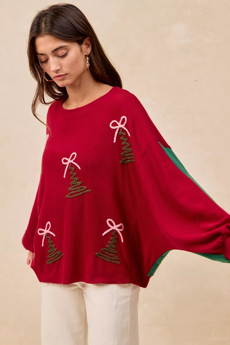 Woman wearing a red Christmas sweater with embroidered green tree designs and contrasting green sleeves.