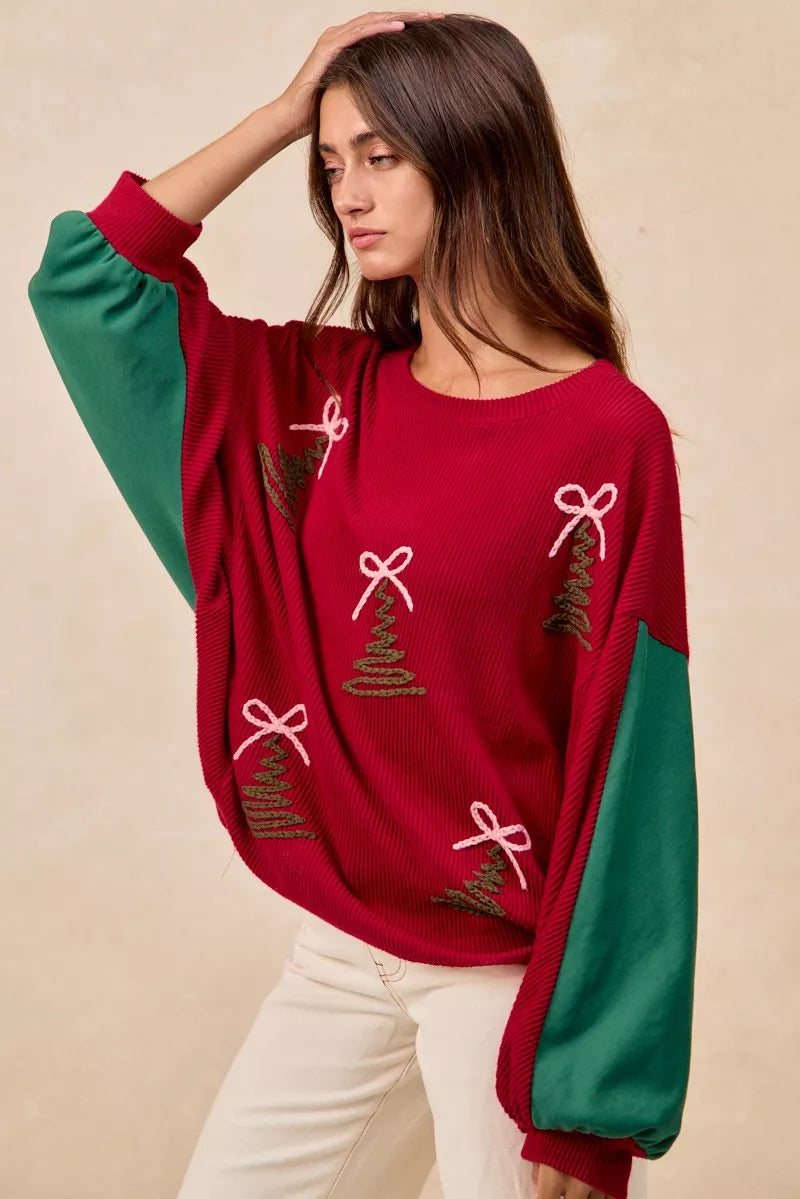 Woman wearing a red Christmas sweater with embroidered green tree designs and contrasting green sleeves.