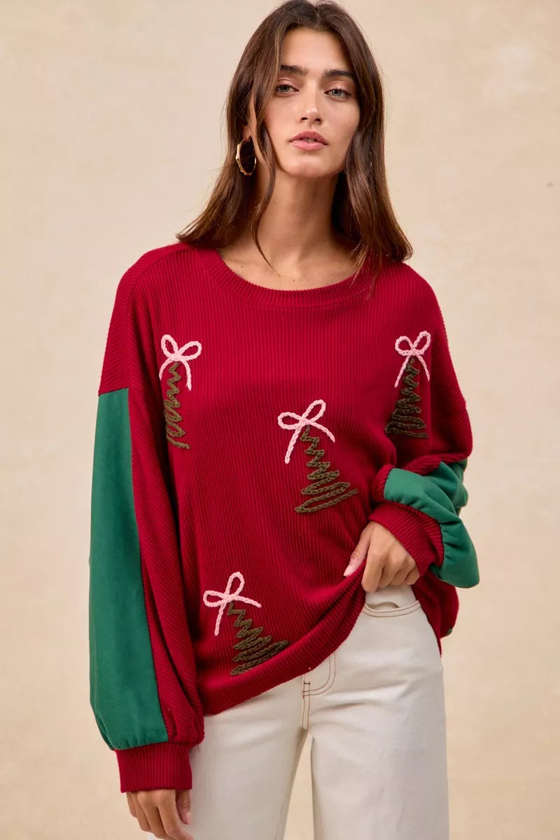 Woman wearing a red Christmas sweater with embroidered green tree designs and contrasting green sleeves.