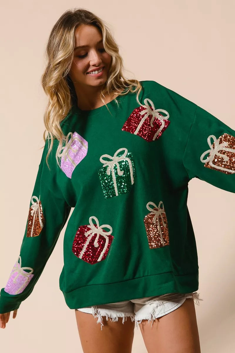 Green Christmas sweatshirt with colorful sequin gift box designs on model with denim shorts