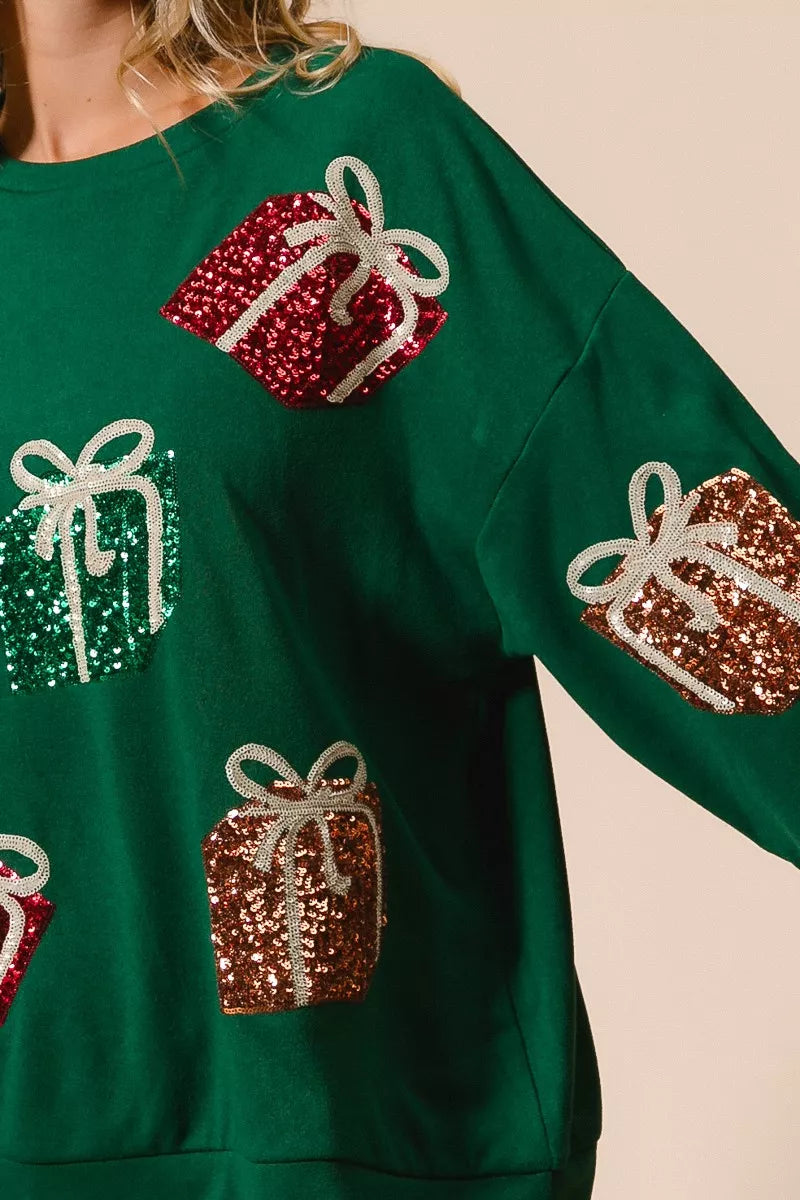 Green Christmas sweatshirt with colorful sequin gift box designs on model with denim shorts