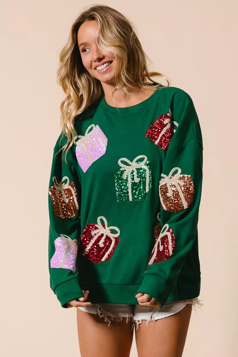 Green Christmas sweatshirt with colorful sequin gift box designs on model with denim shorts