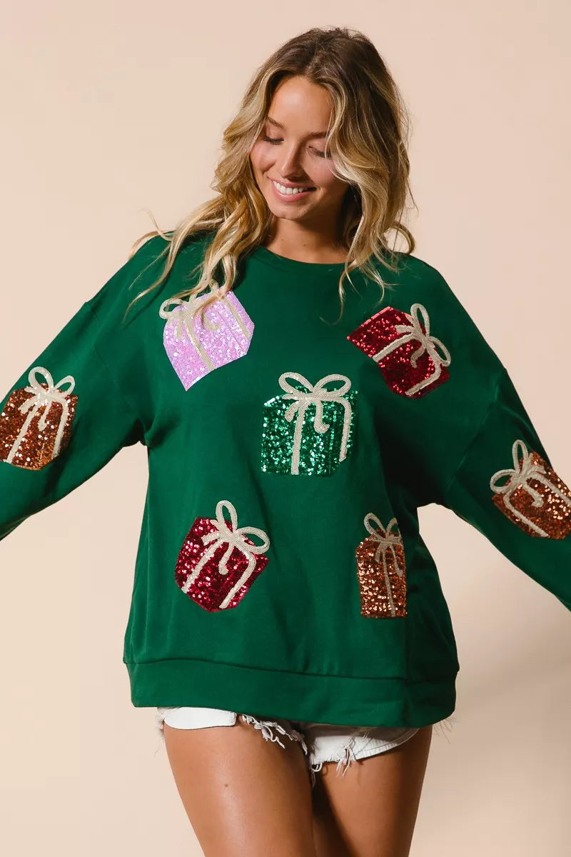 Green Christmas sweatshirt with colorful sequin gift box designs on model with denim shorts