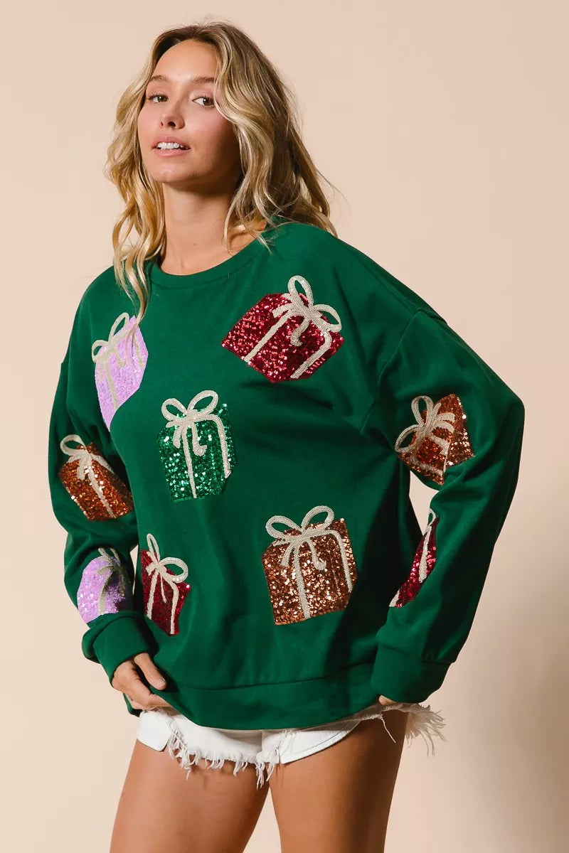 Green Christmas sweatshirt with colorful sequin gift box designs on model with denim shorts