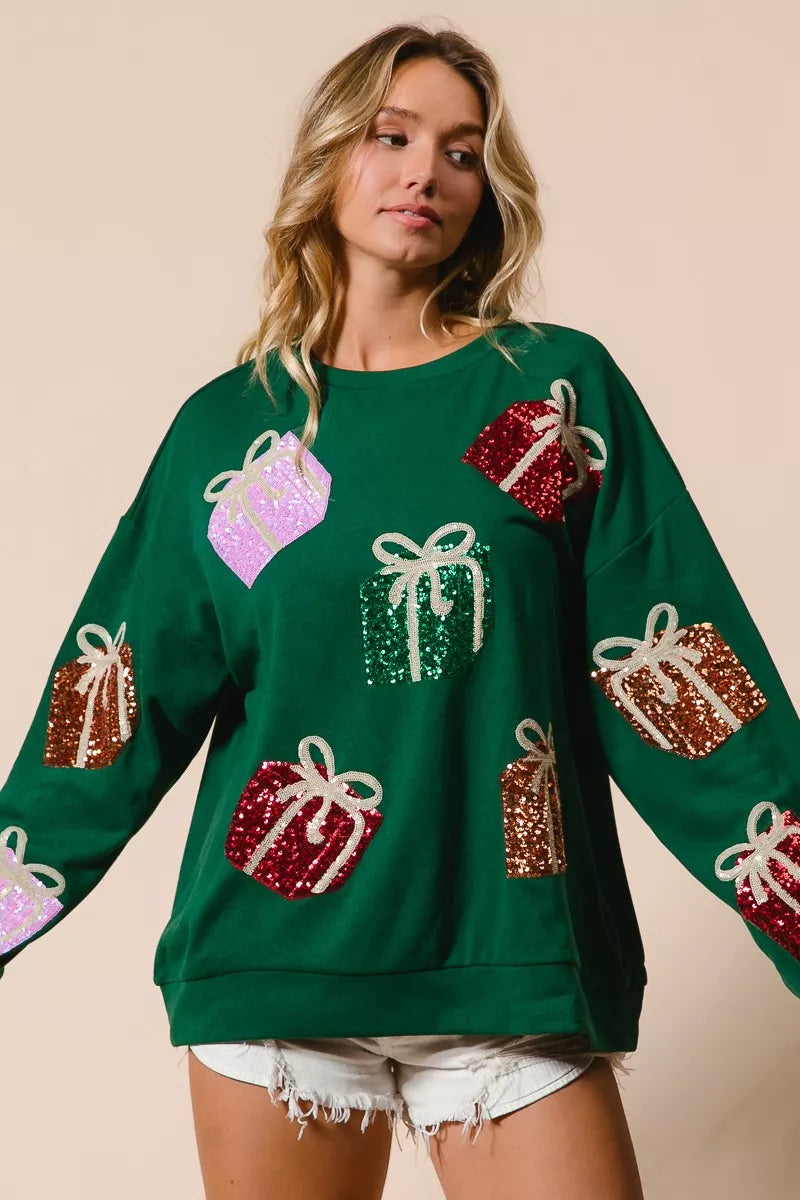 Green Christmas sweatshirt with colorful sequin gift box designs on model with denim shorts
