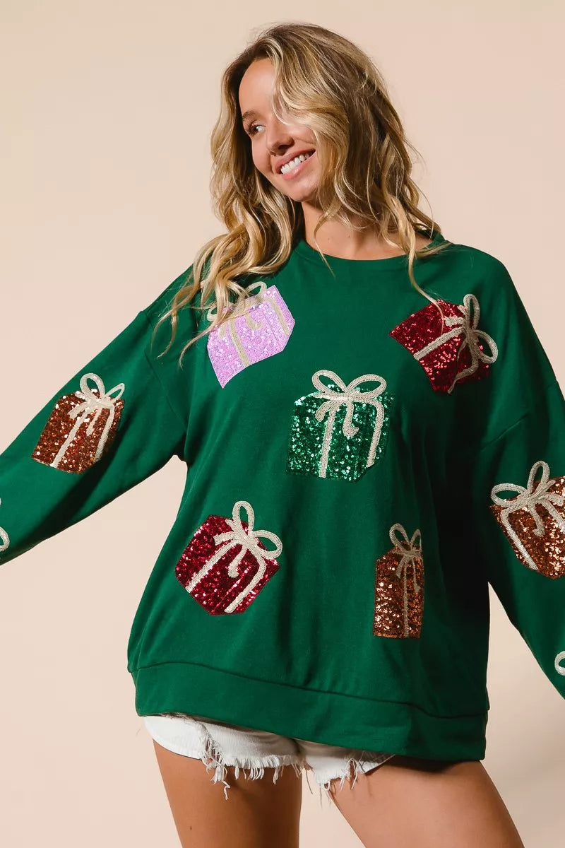 Green Christmas sweatshirt with colorful sequin gift box designs on model with denim shorts