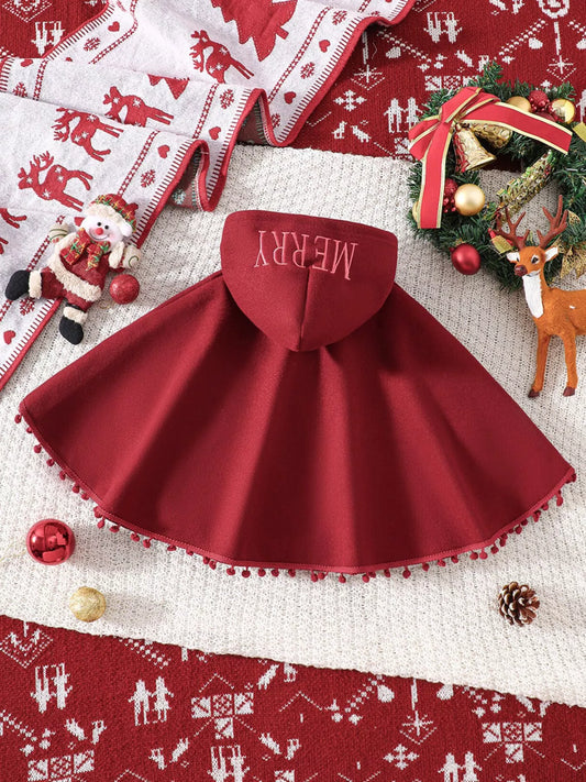 Red Christmas hooded cape for kids with “MERRY” embroidery and reindeer appliqués, pom-trim hem, displayed on holiday background.