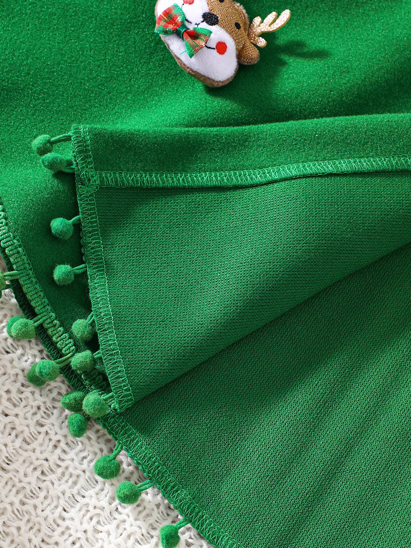 Green Christmas hooded cape for kids with “MERRY” embroidery and reindeer appliqués, pom-trim hem, displayed on holiday background.
