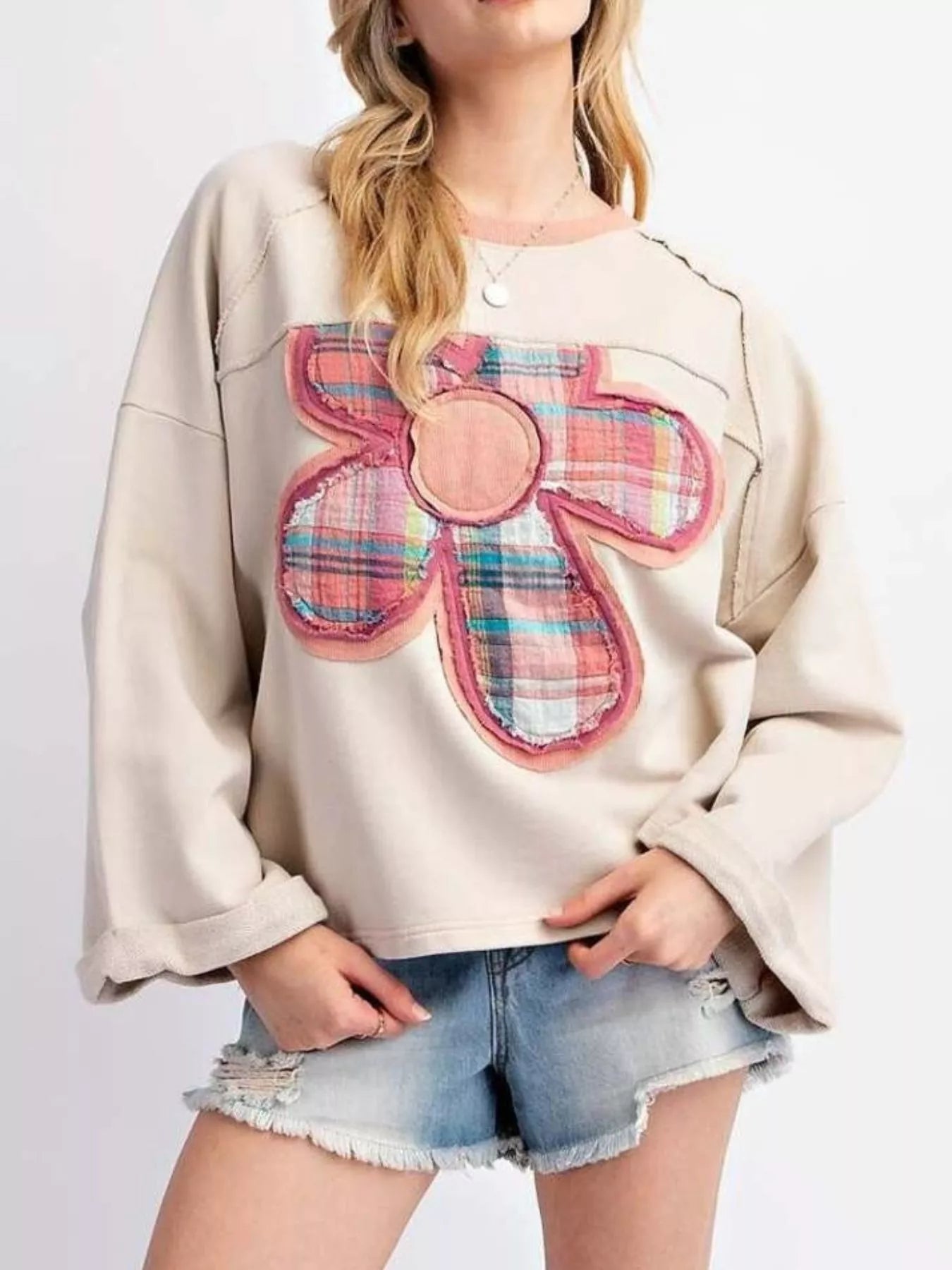 Beige pullover featuring a pink plaid flower patch, paired with distressed denim shorts.