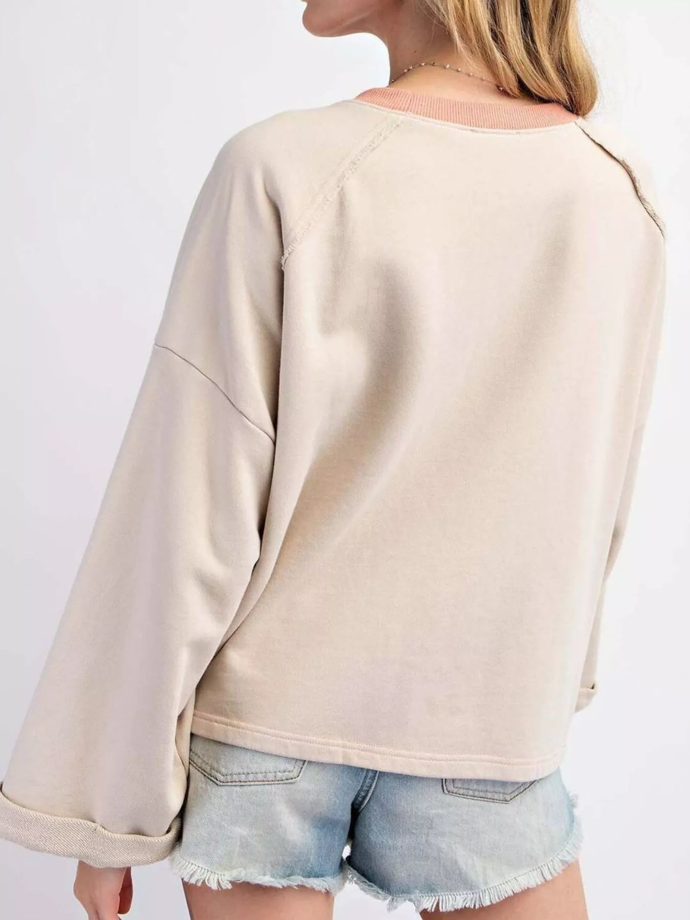 Beige pullover featuring a pink plaid flower patch, paired with distressed denim shorts.