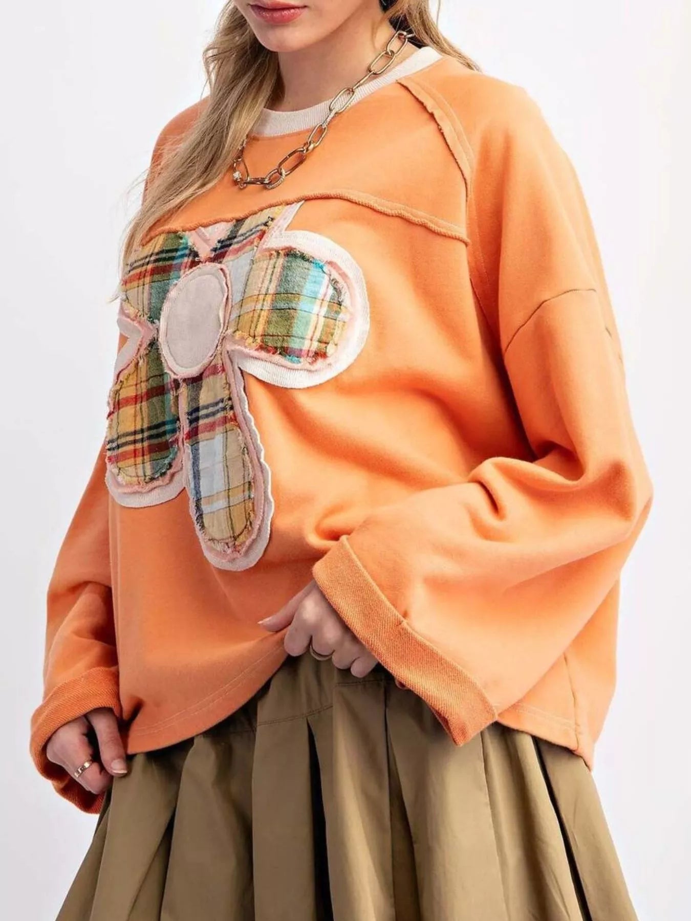 Bright orange pullover with plaid flower appliqué, styled with a pleated khaki skirt.