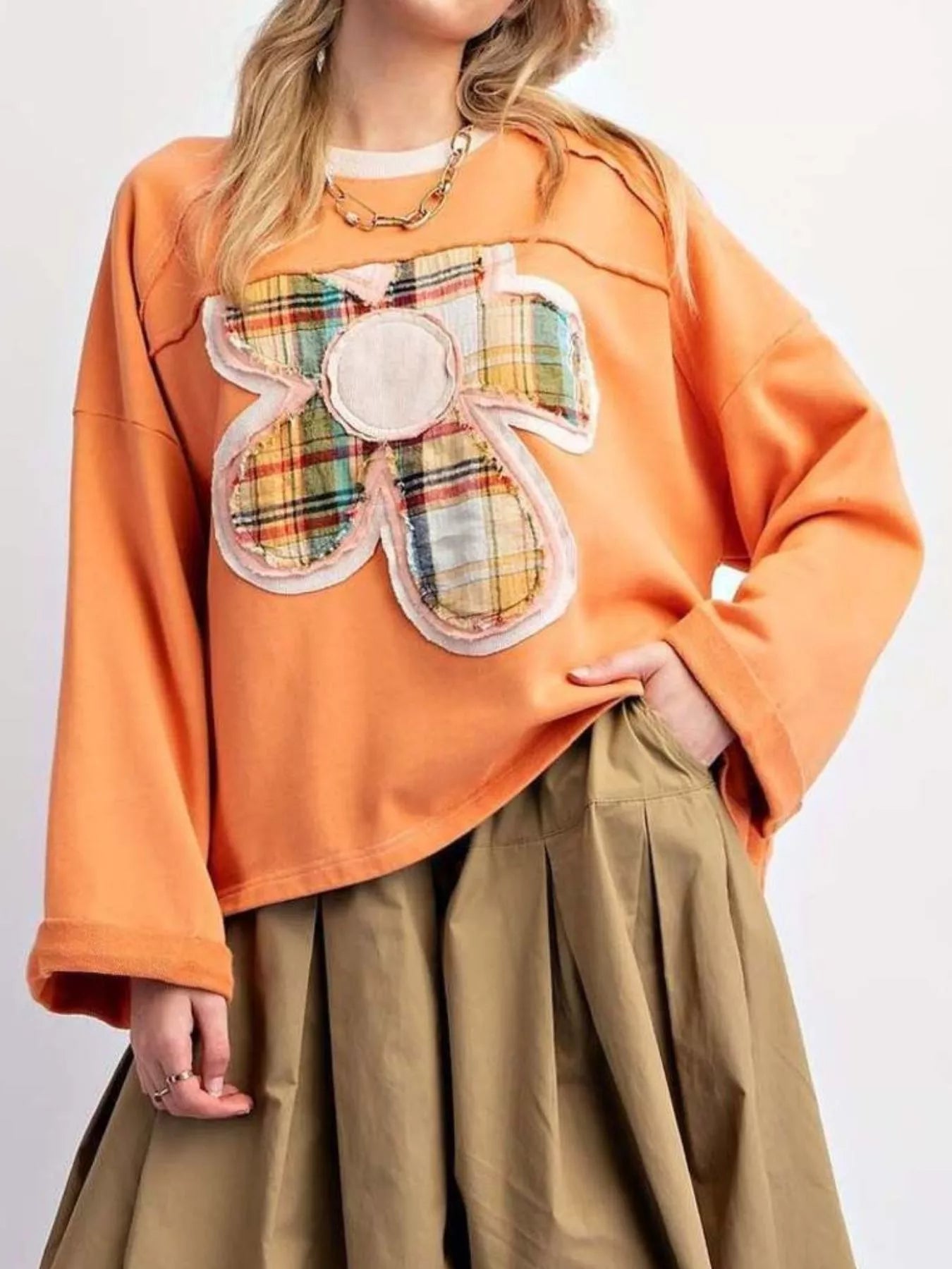 Bright orange pullover with plaid flower appliqué, styled with a pleated khaki skirt.