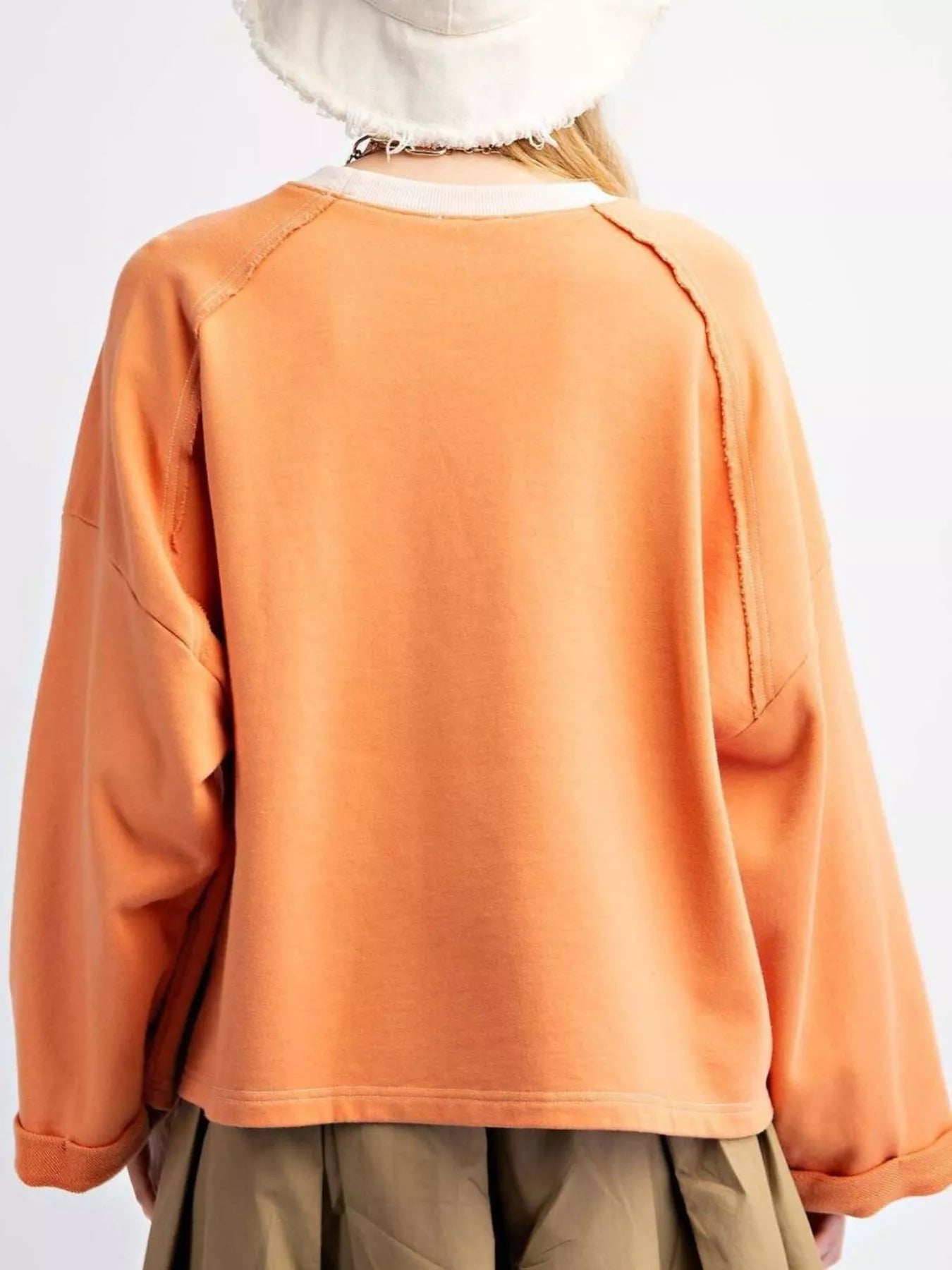 Bright orange pullover with plaid flower appliqué, styled with a pleated khaki skirt.