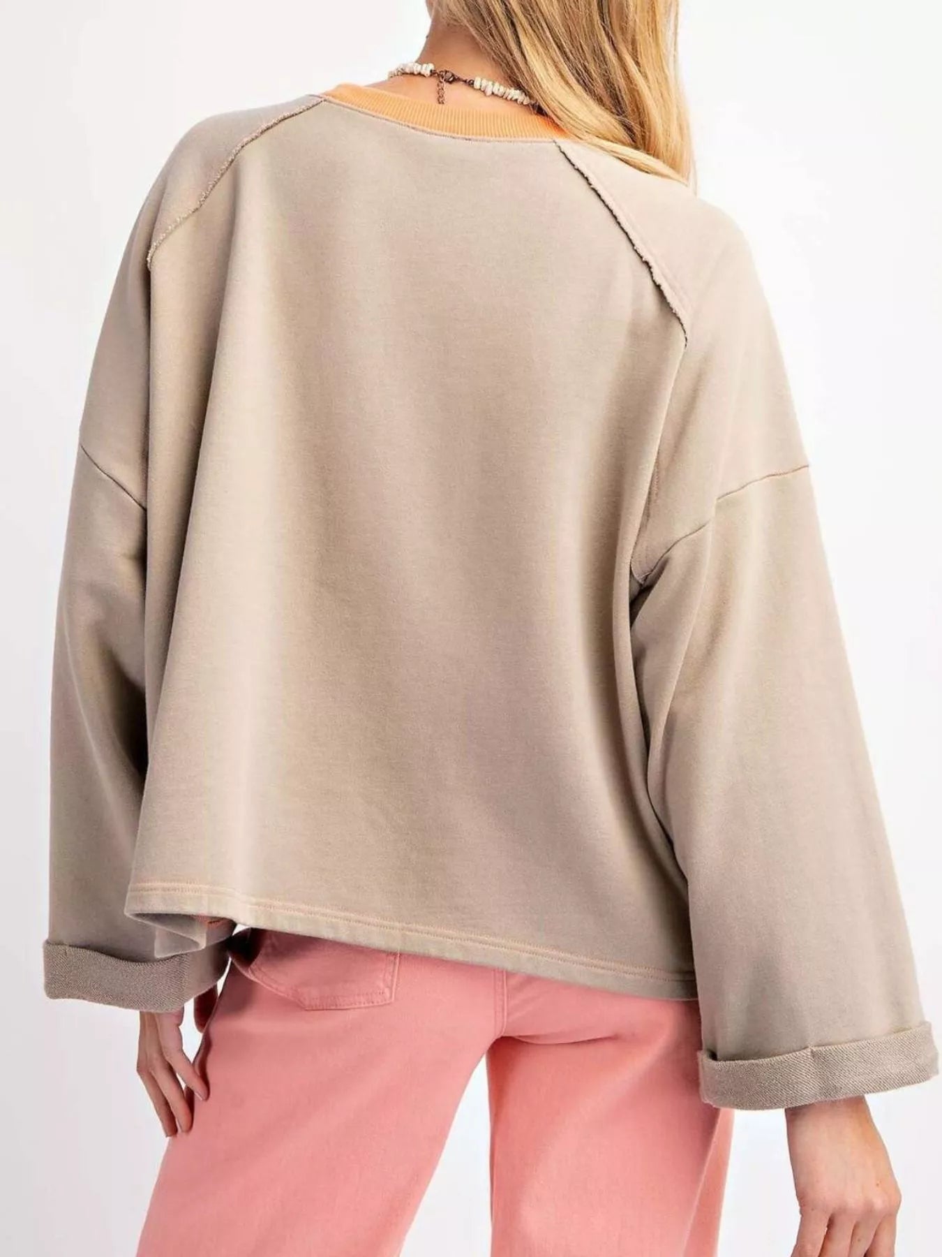 Taupe pullover with oversized plaid flower appliqué in orange tones, styled with light pink pants.
