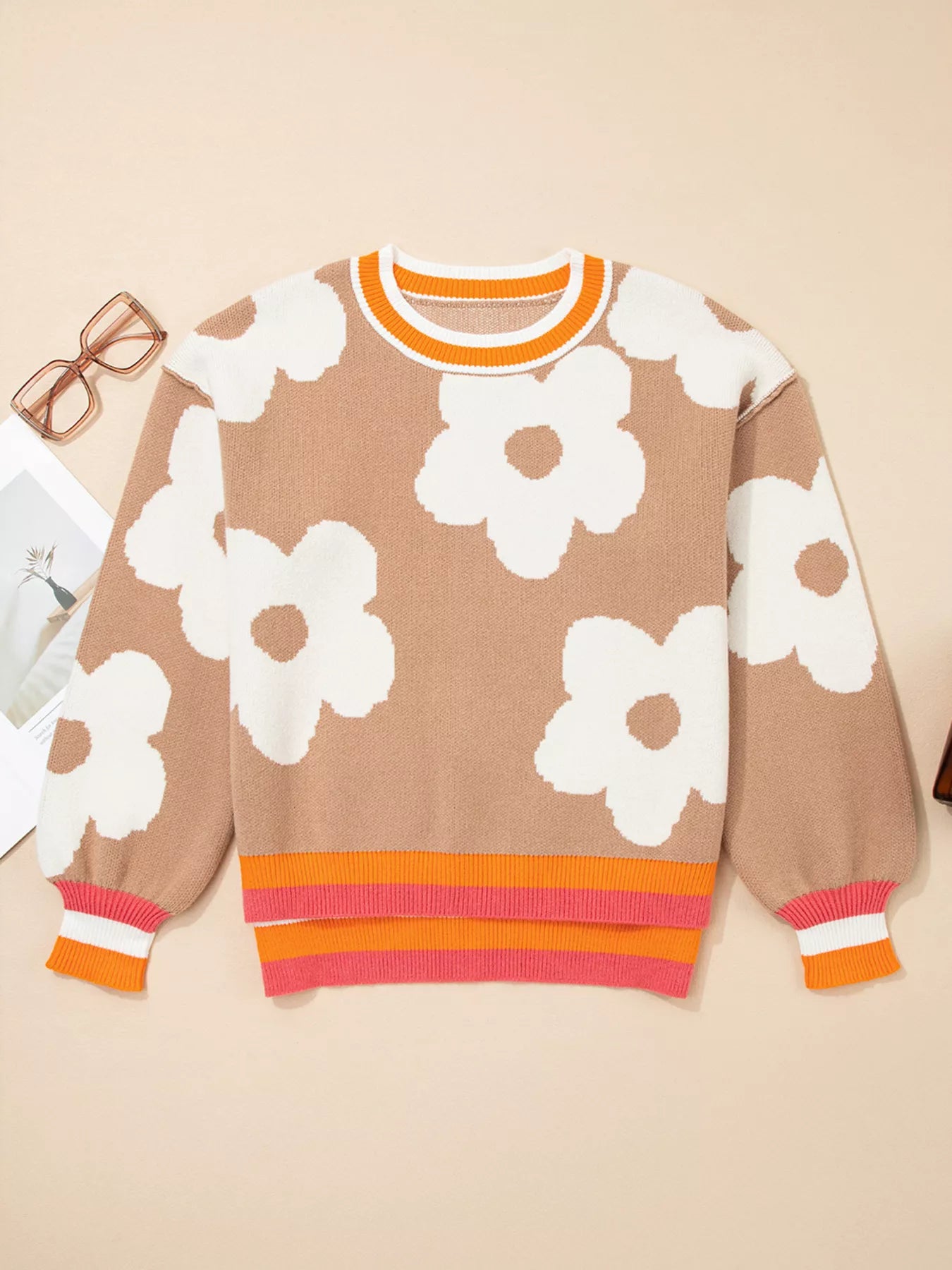 Woman wearing beige sweater with oversized white daisy flowers and orange trim