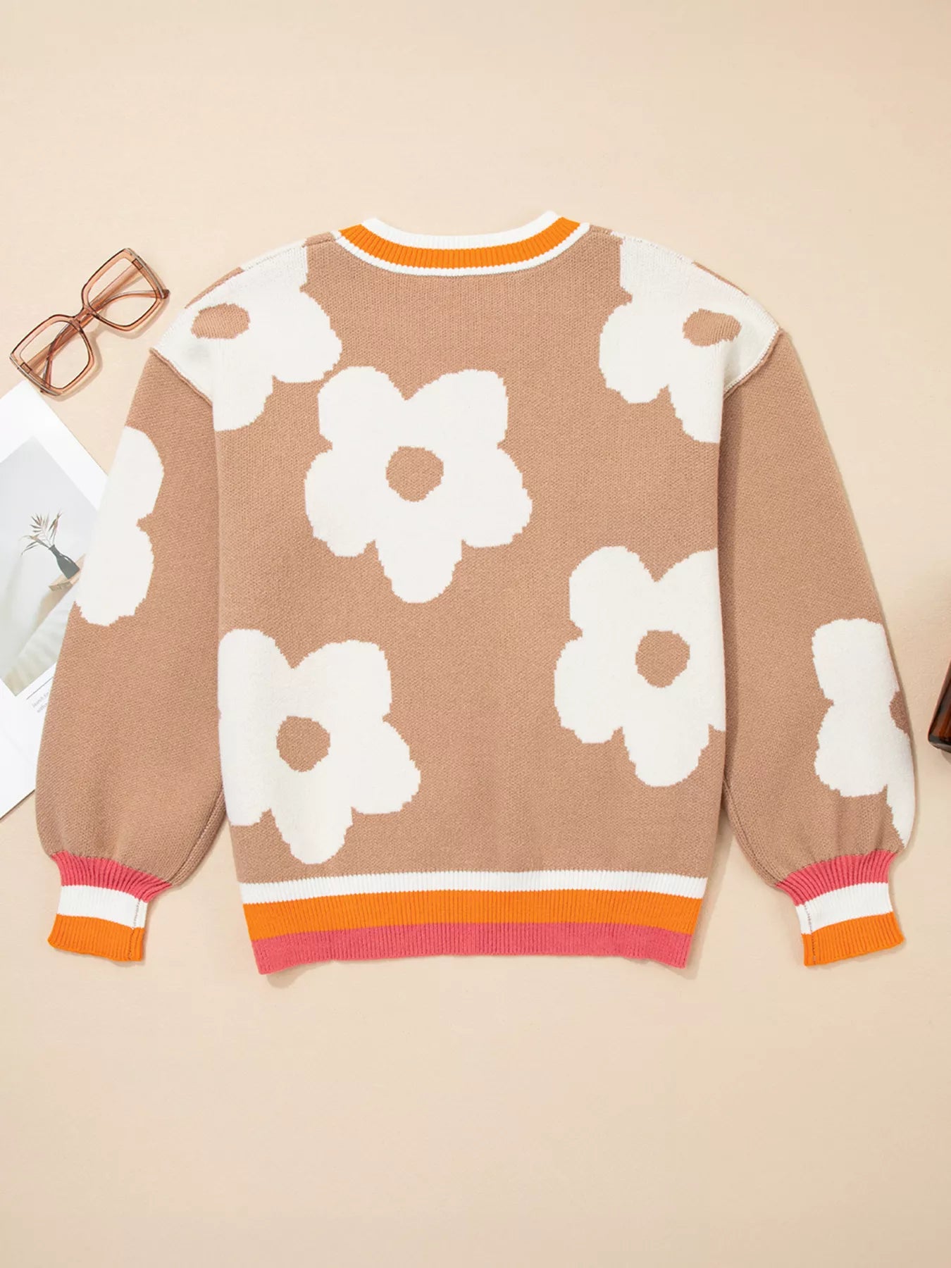 Woman wearing beige sweater with oversized white daisy flowers and orange trim