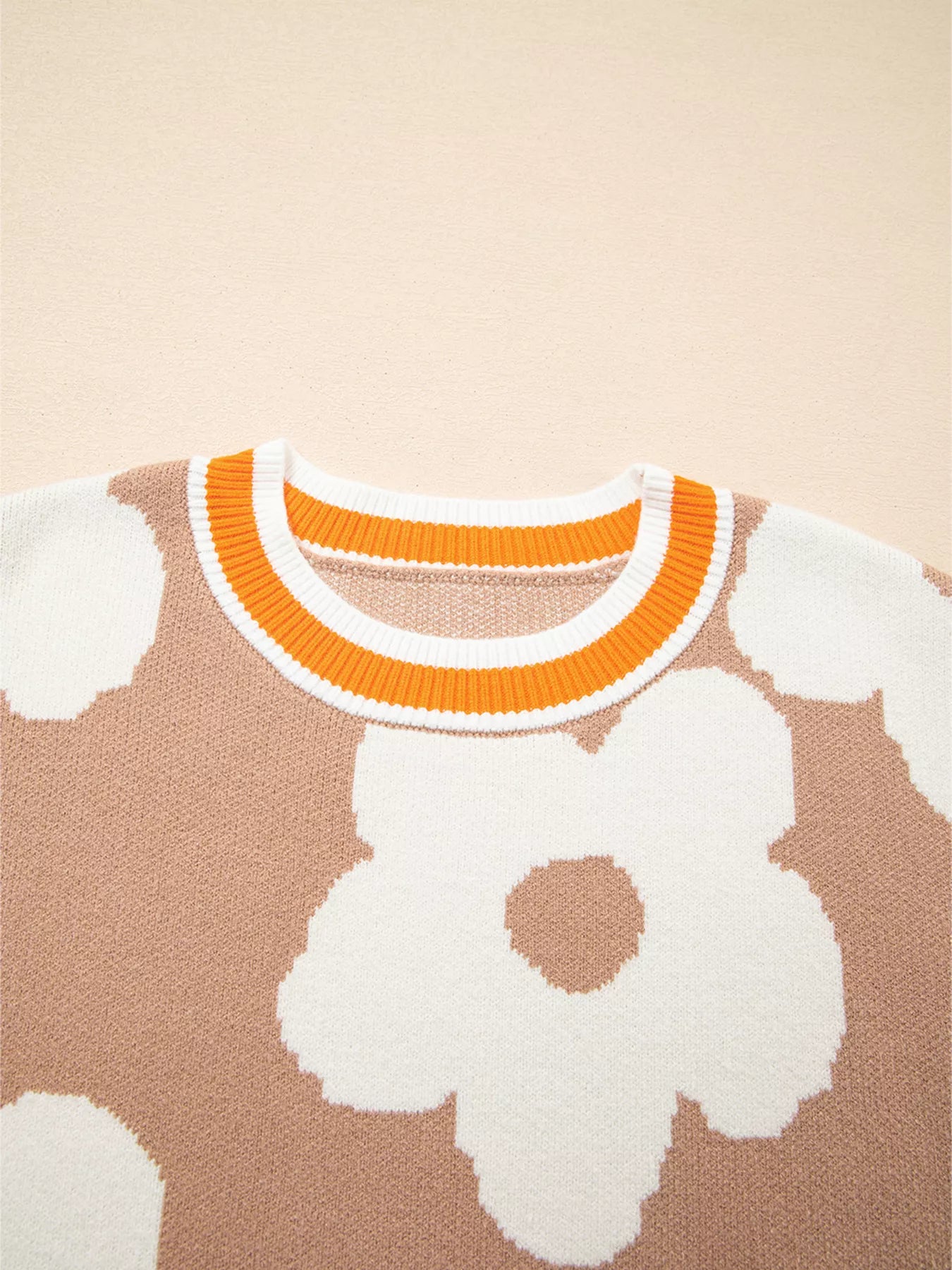 Woman wearing beige sweater with oversized white daisy flowers and orange trim