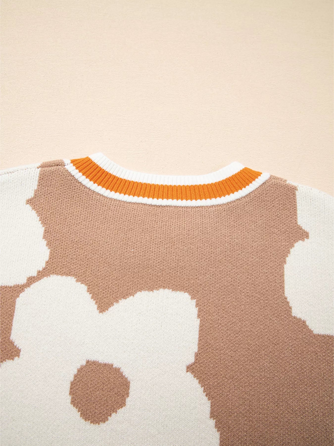 Woman wearing beige sweater with oversized white daisy flowers and orange trim