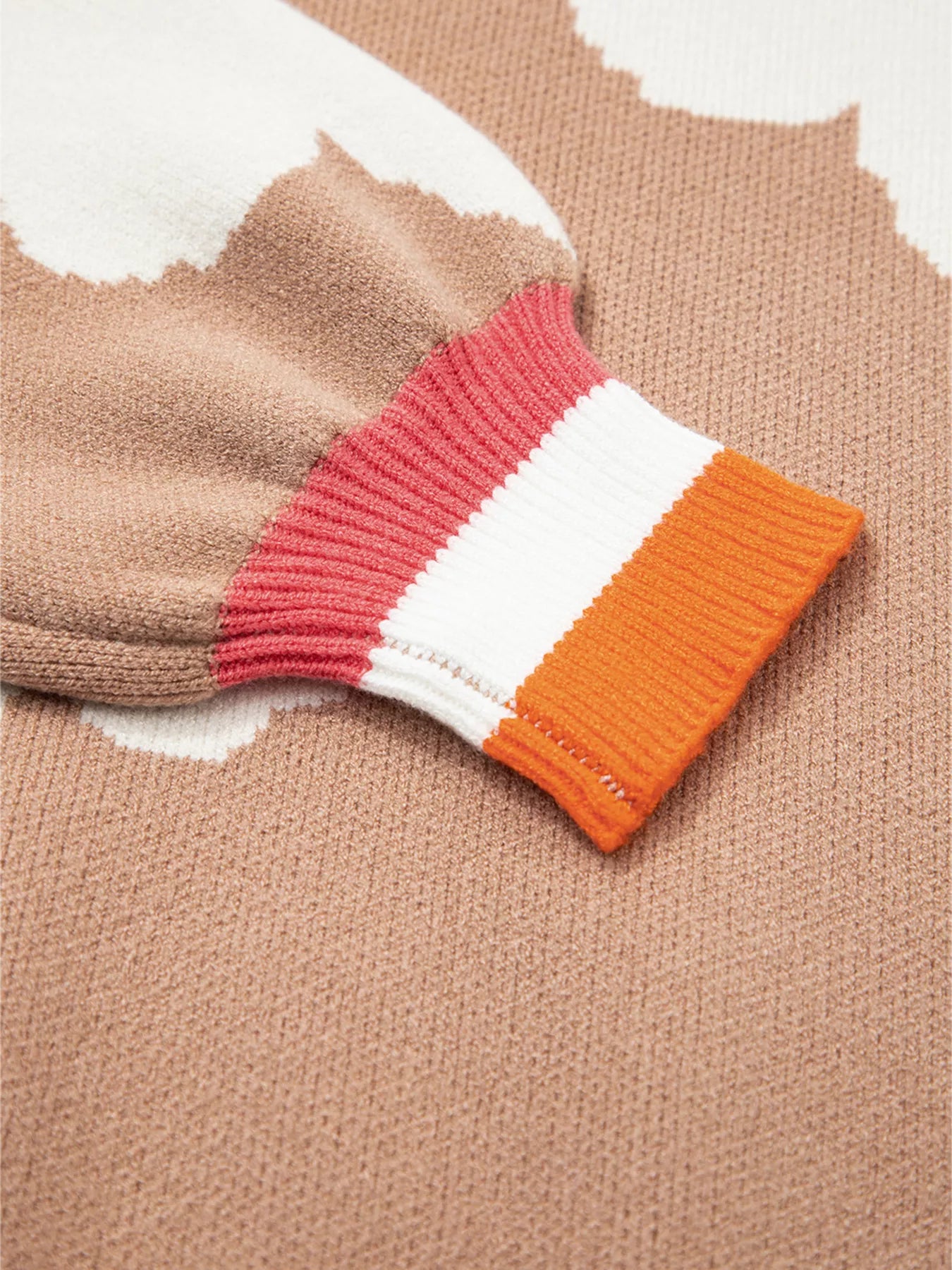 Woman wearing beige sweater with oversized white daisy flowers and orange trim