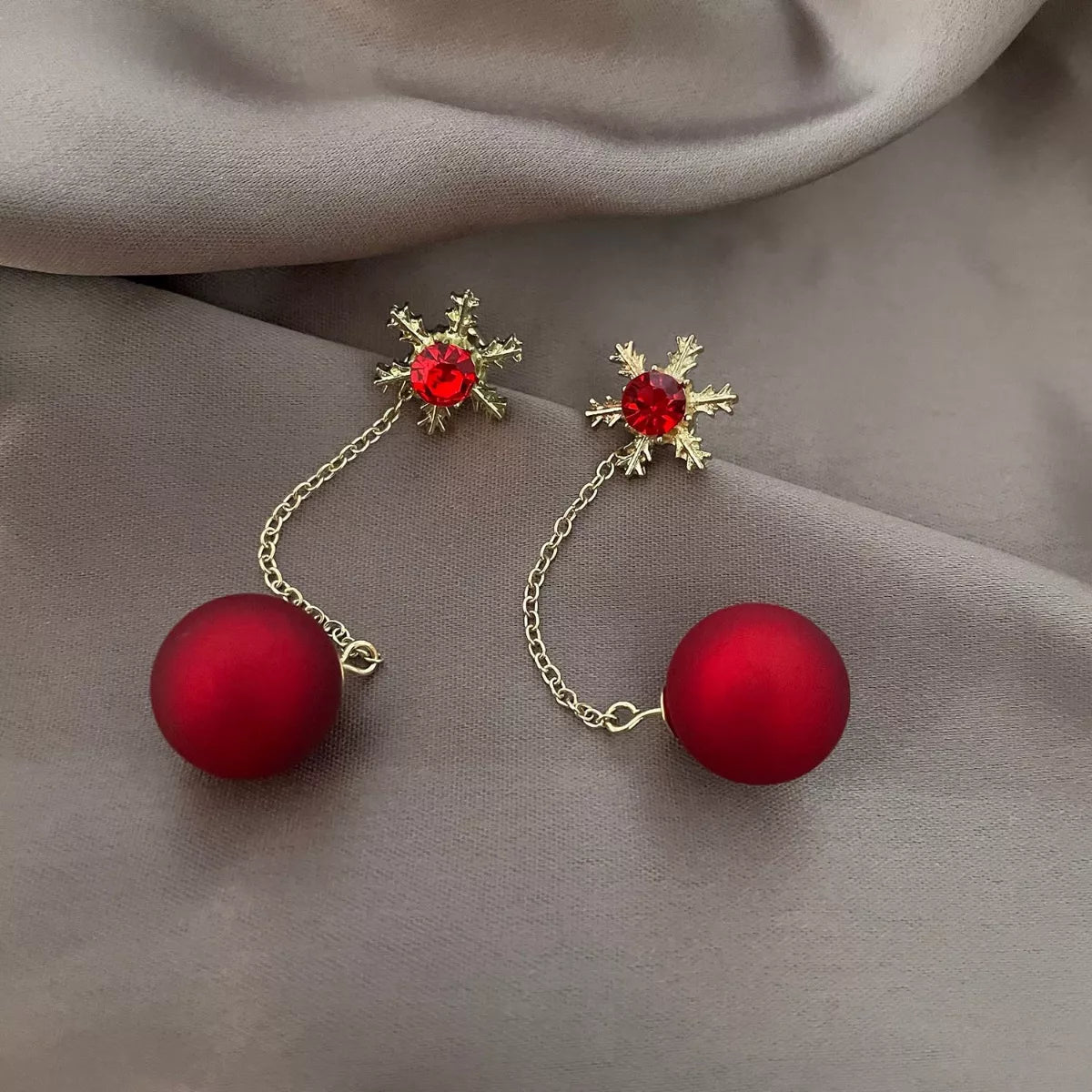 Festive red bauble drop earrings with snowflake studs and gold chain detailing.