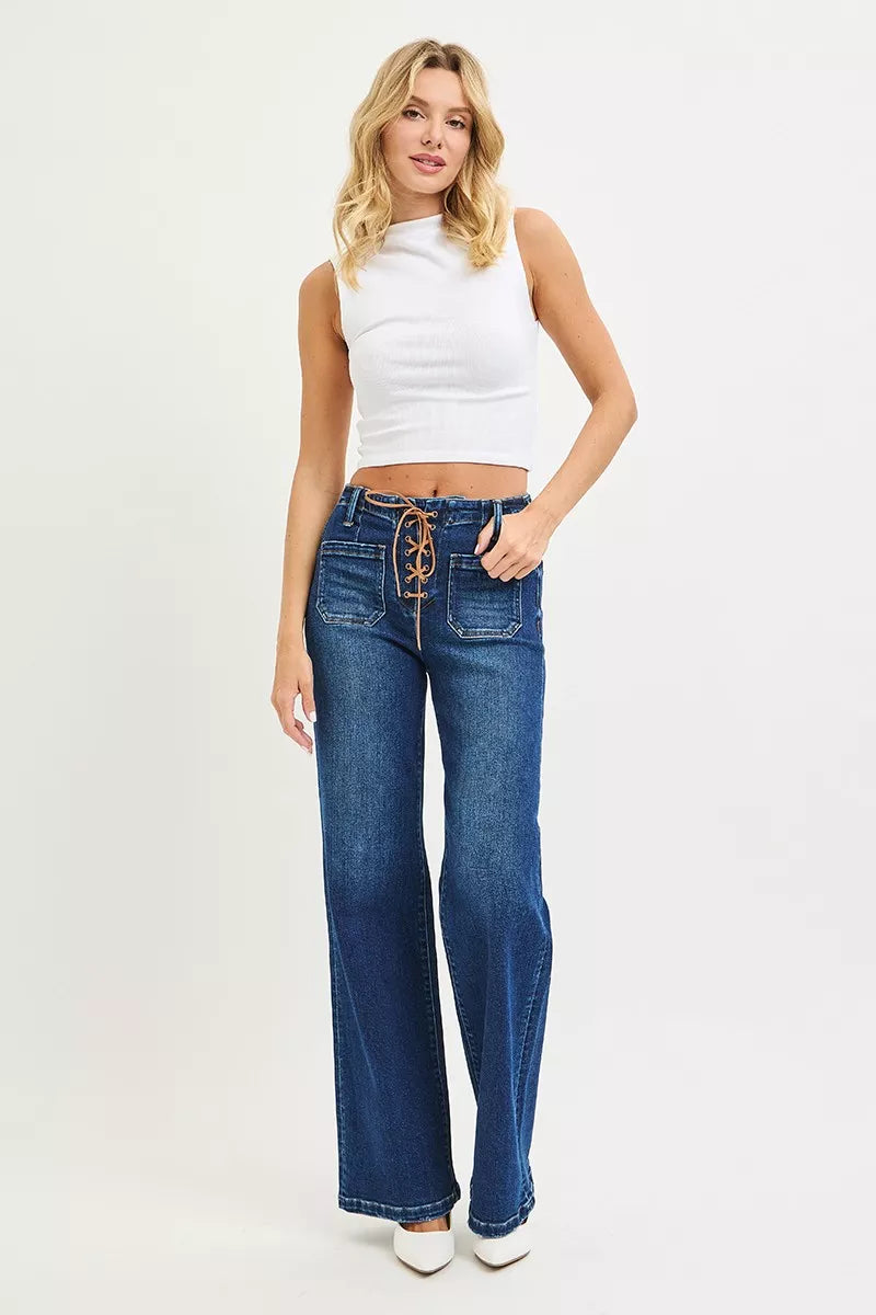 High-rise wide leg jeans with a tan lace-up front detail and front patch pockets, shown on a model wearing white heels.
