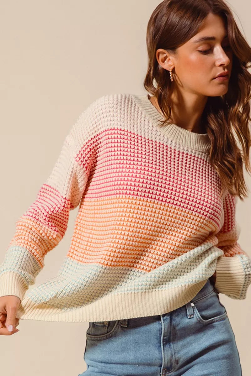 Woman wearing a pastel color block waffle-knit sweater in pink, orange, and blue tones — cozy ribbed pullover from A Whimsical Affair.