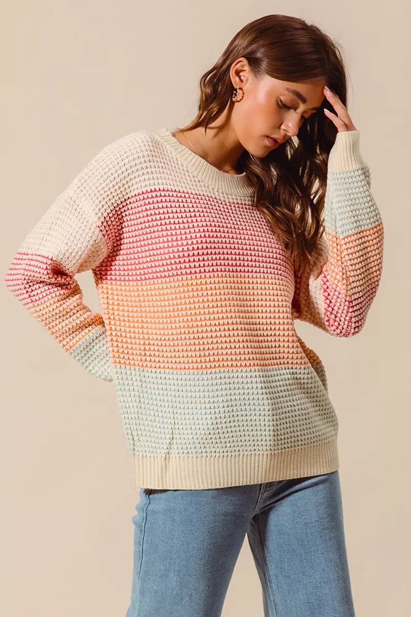 Woman wearing a pastel color block waffle-knit sweater in pink, orange, and blue tones — cozy ribbed pullover from A Whimsical Affair.